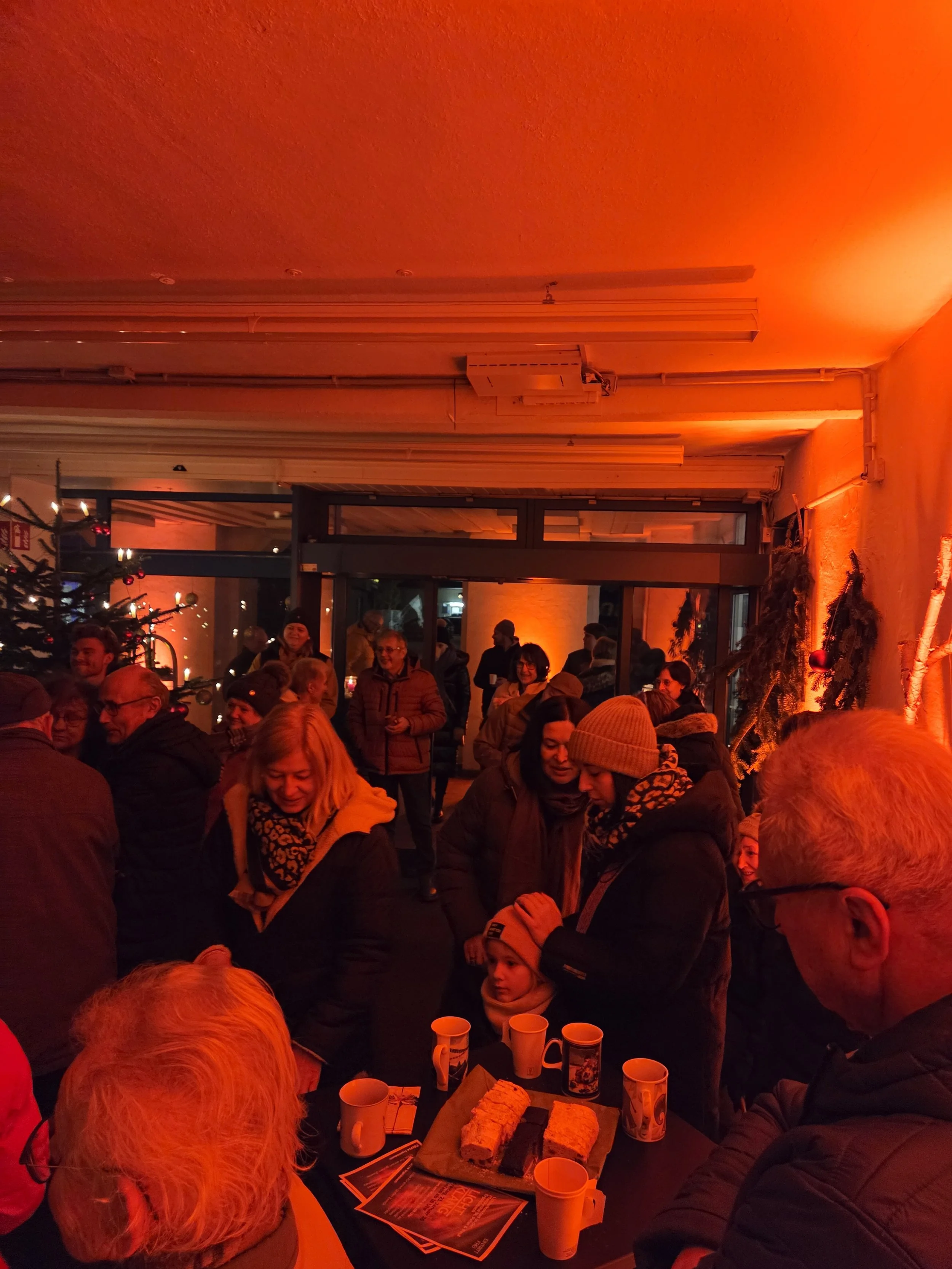 Menschen versammelt sich bei einer Weihnachtsfeier in einem Raum mit Weihnachtsdekoration und einem Tisch mit Kuchen und Getränken.