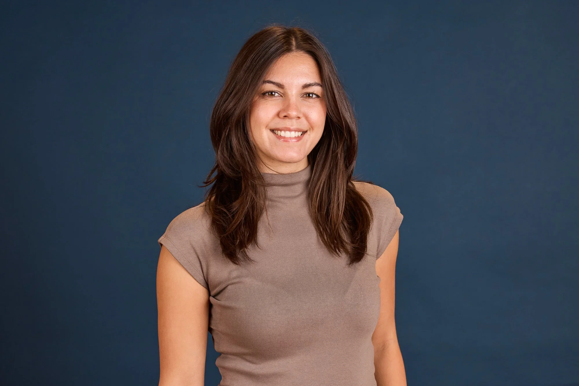 Porträt einer lächelnden jungen Frau mit braunen, schulterlangen Haaren vor einem dunklen blauen Hintergrund.