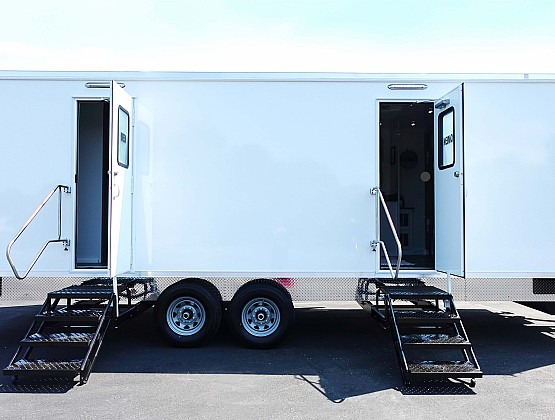 Two white mobile trailers with open doors and black stairs leading inside, parked on a paved surface.