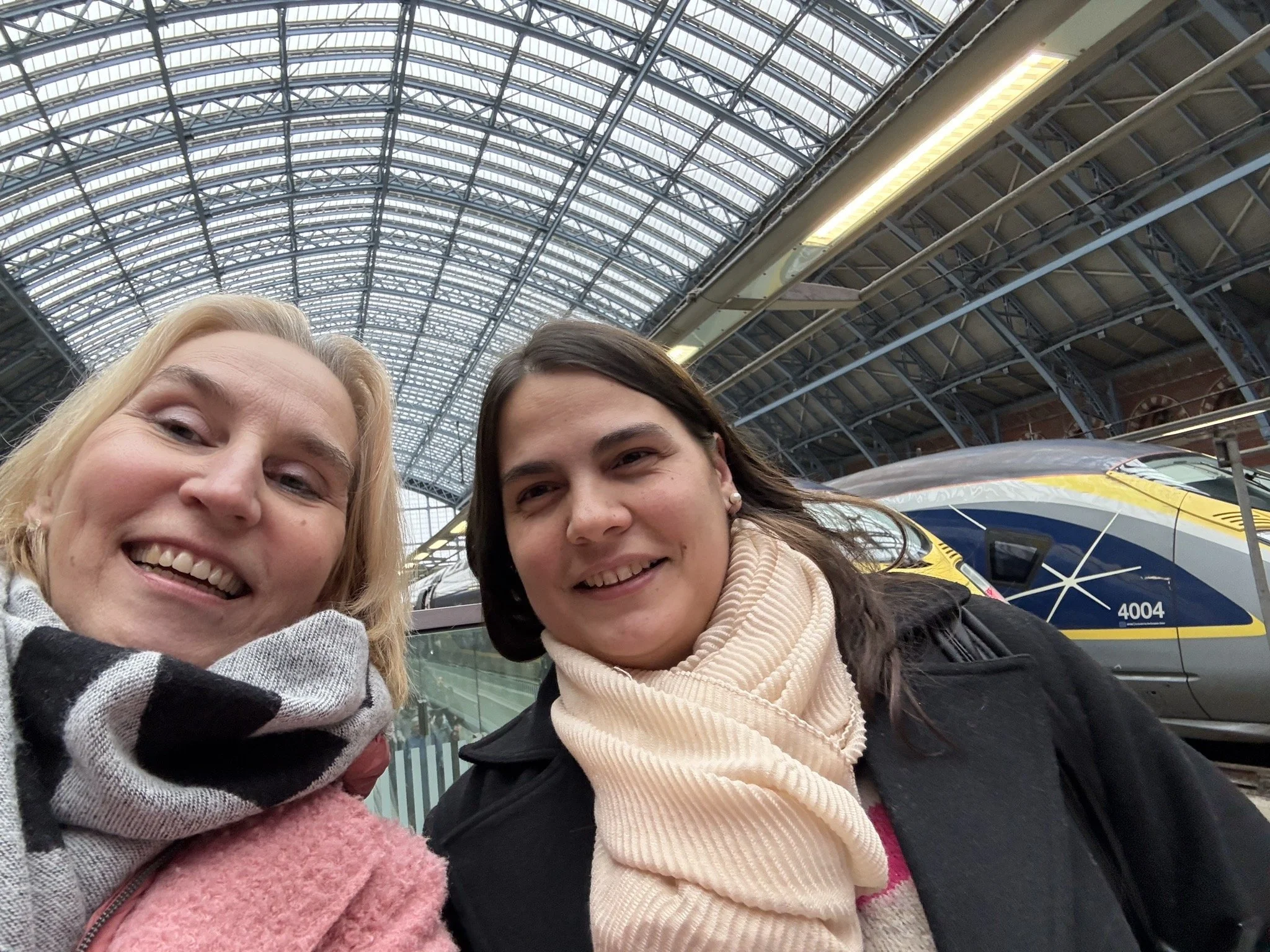 Two women taking a selfie at a train station with a modern train in the background.