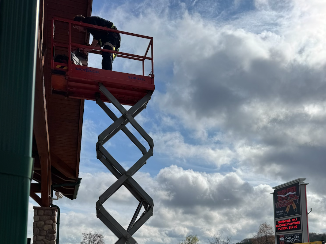 Worker on a red lift platform working on the exterior of a building against a cloudy sky.