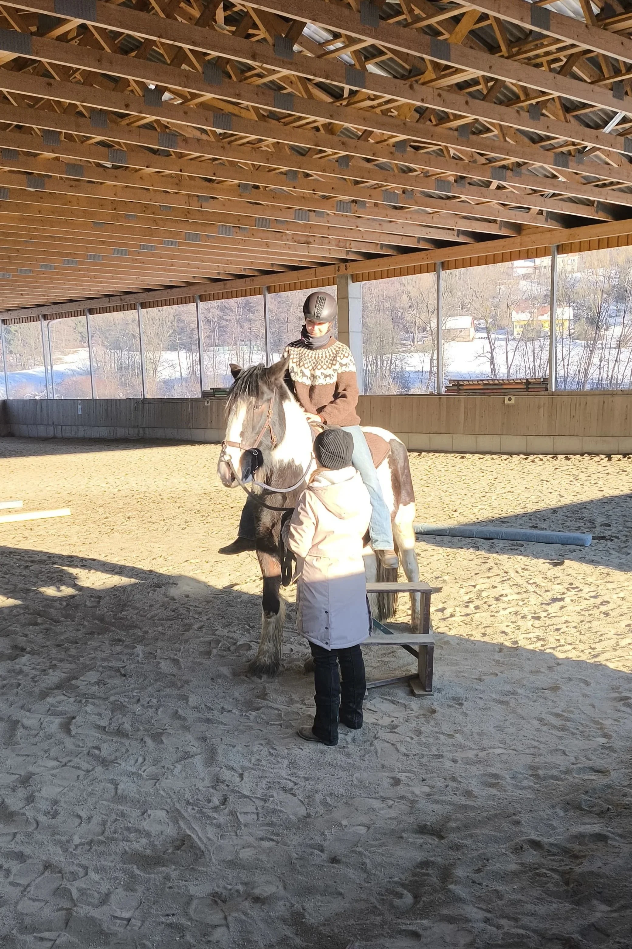 Menschen, die auf einem Pferd in einer Indoor-Reithalle reiten, mit einem Begleiter, der ihnen Anweisungen gibt.
