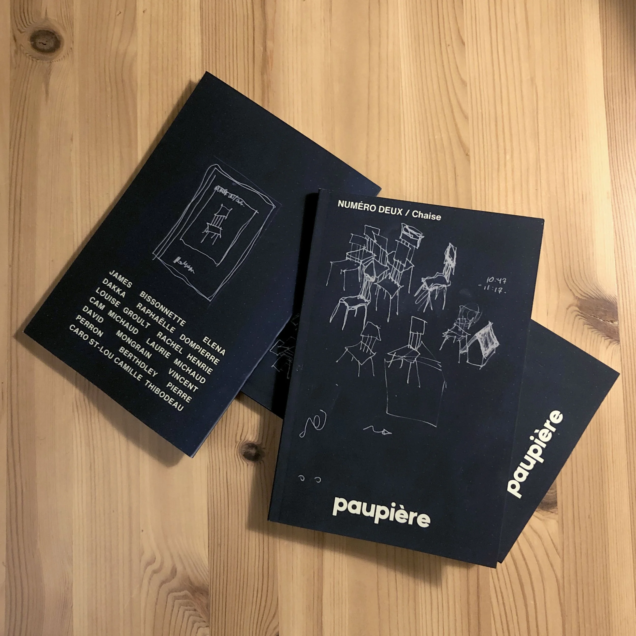 Deux brochures de programmes artistiques, une avec une illustration d'une chaise et une autre avec une illustration de plusieurs chaises, posées sur une surface en bois.