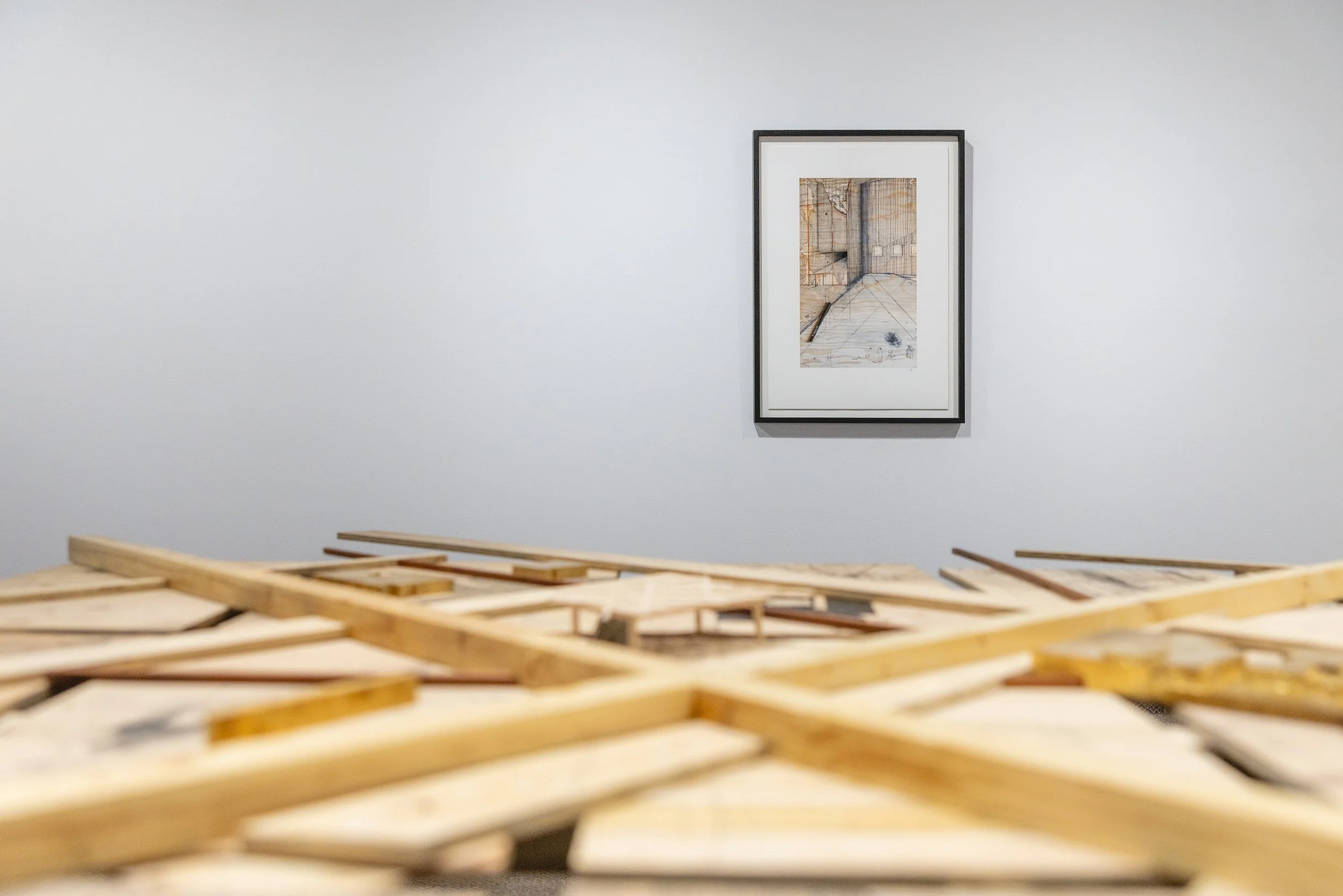 Une installation artistique avec des morceaux de bois en premier plan et une peinture moderne en arrière-plan dans une galerie d'art.