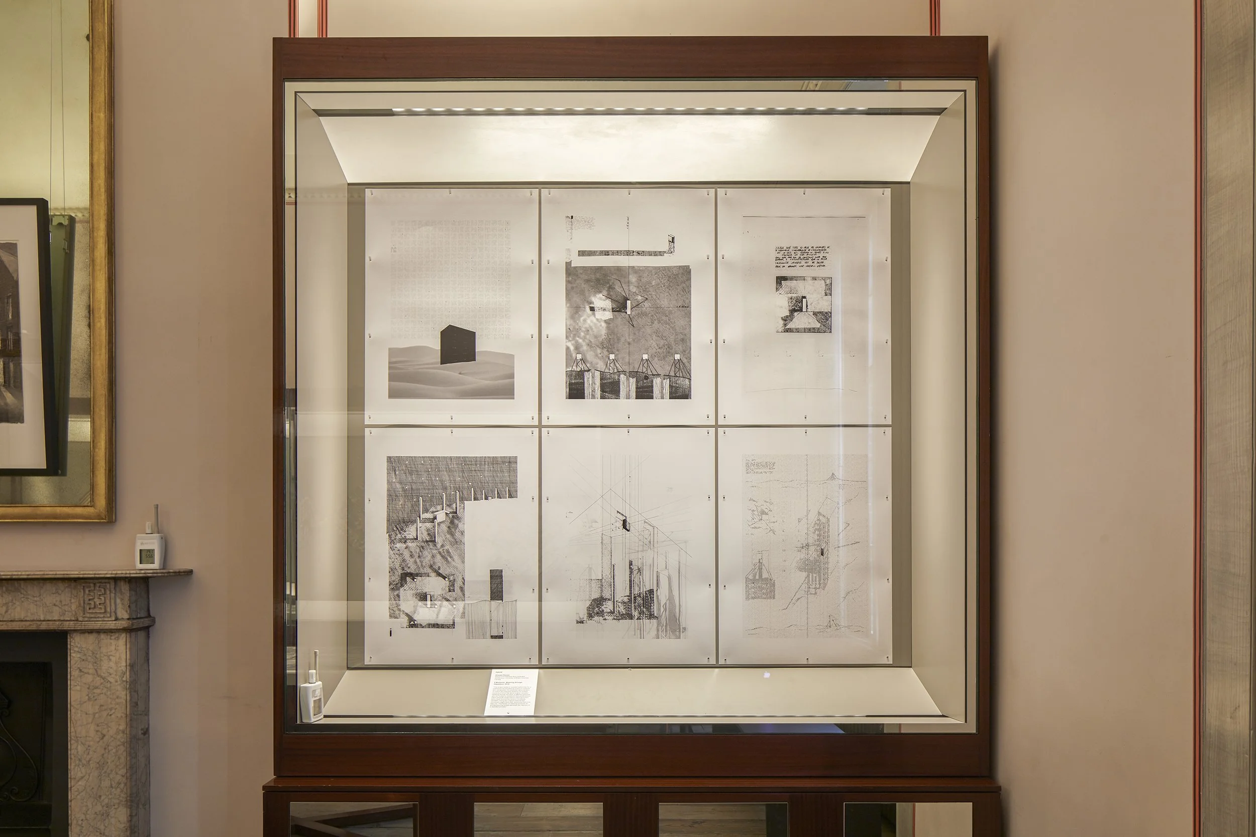 Une vitrine en bois contenant six plans ou dessins architecturaux en noir et blanc, exposés dans une musé