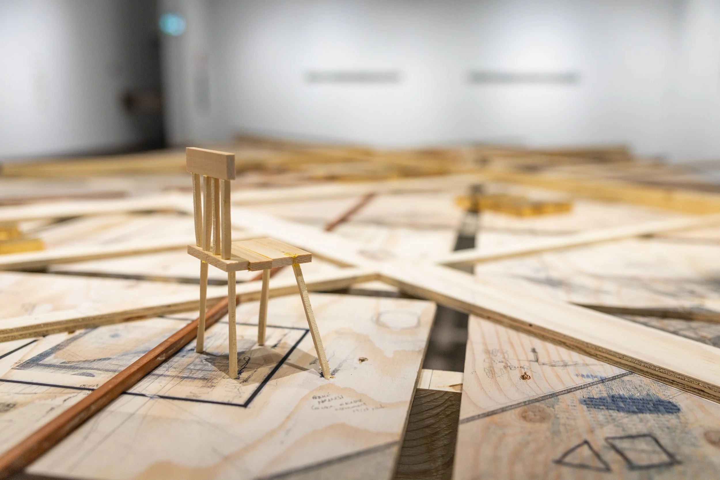 Une maquette en bois représentant une chaise sur un plan de travail de bois, avec d'autres plans et matériaux de construction autour.