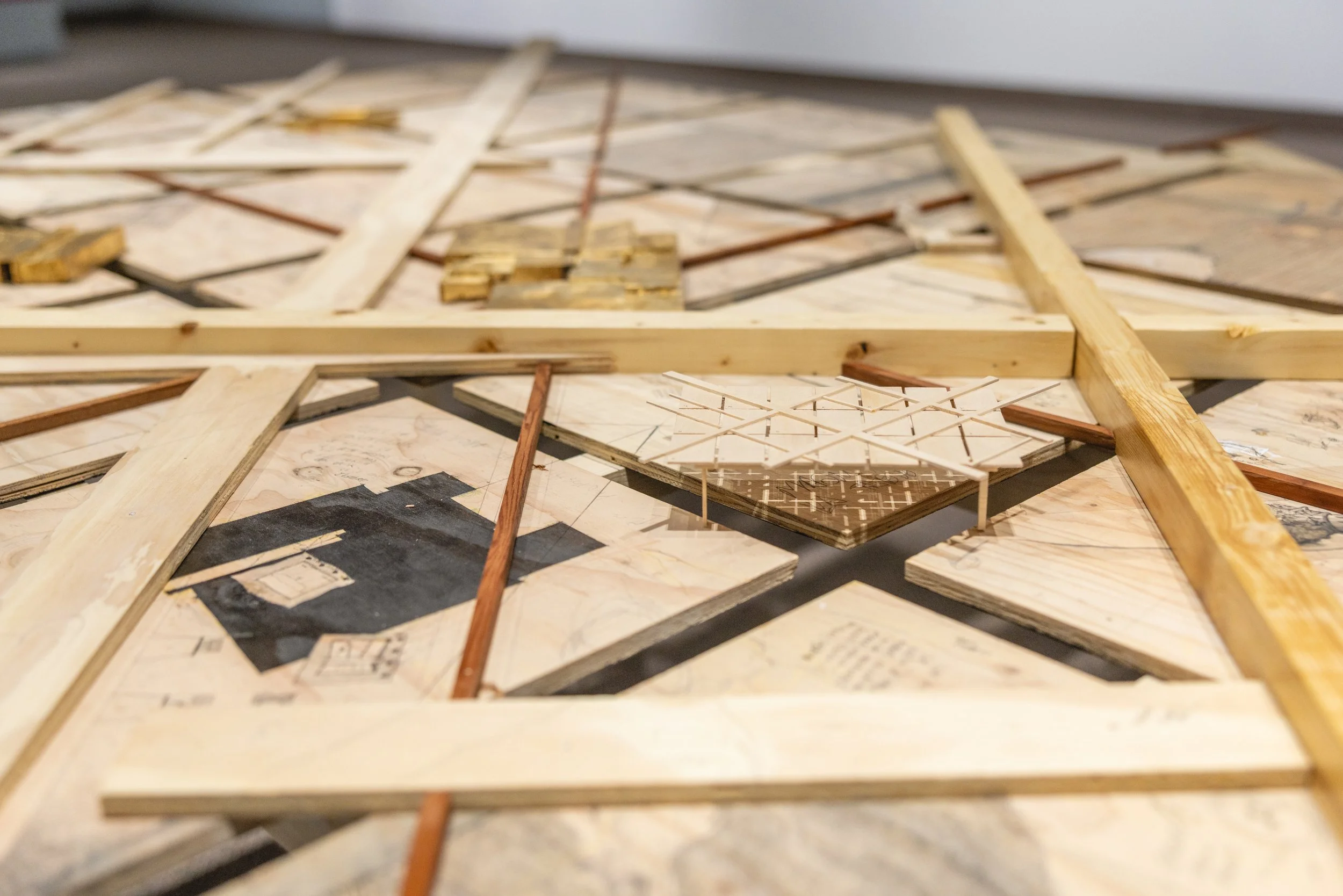 Une composition de divers matériaux en bois et papier, comprenant des planches en bois, de fines bandes de bois, et des morceaux de papier avec des dessins ou schémas.