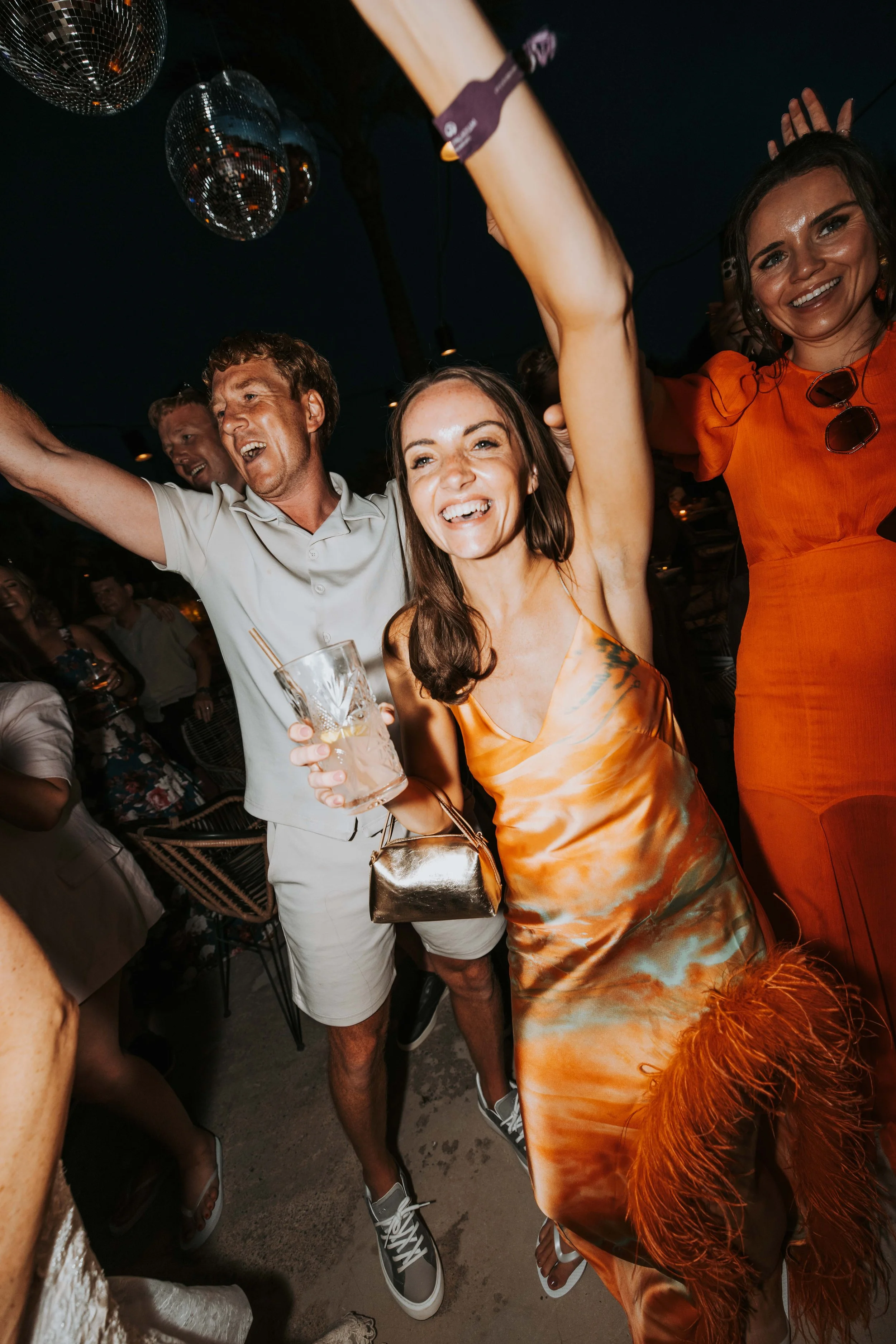 Group of people celebrating at a party, smiling and dancing. Disco balls hanging from the ceiling in the background.