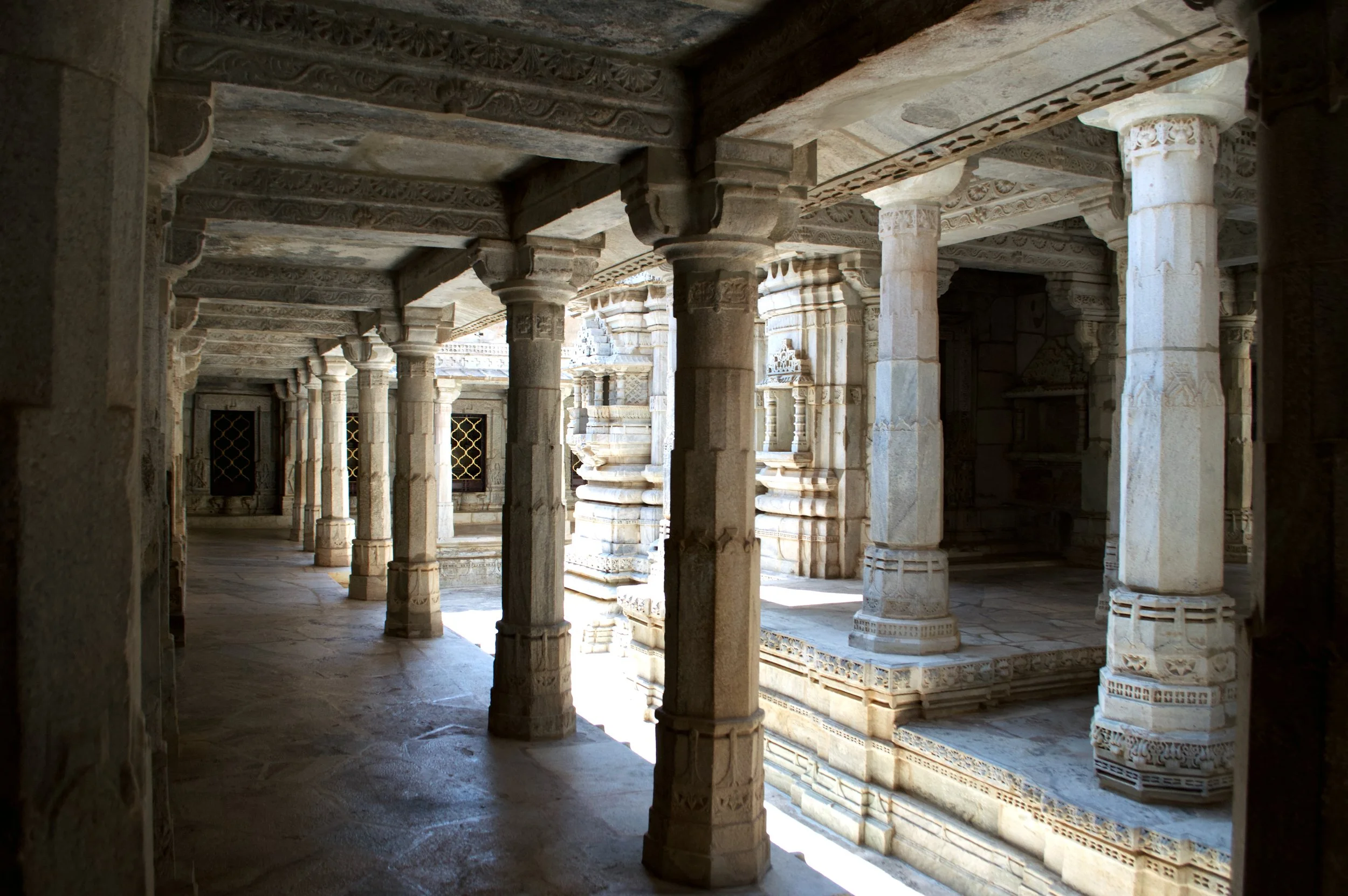 Interior di un tempio indù con colonne di pietra scolpita, archi e decorazioni dettagliate, illuminato dalla luce naturale.