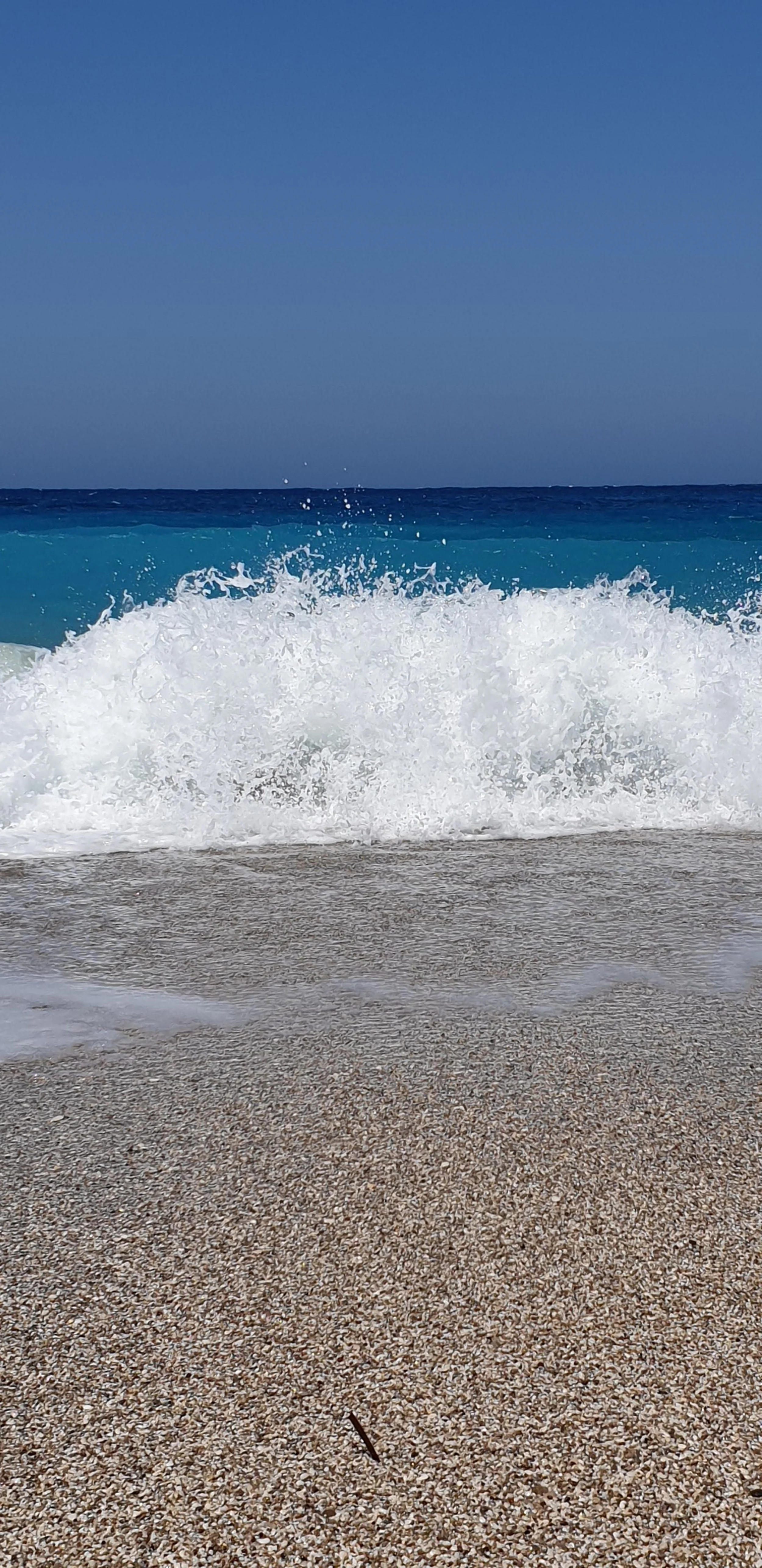 Ondata che si infrange sulla spiaggia di sabbia con il mare blu e il cielo azzurro in background.