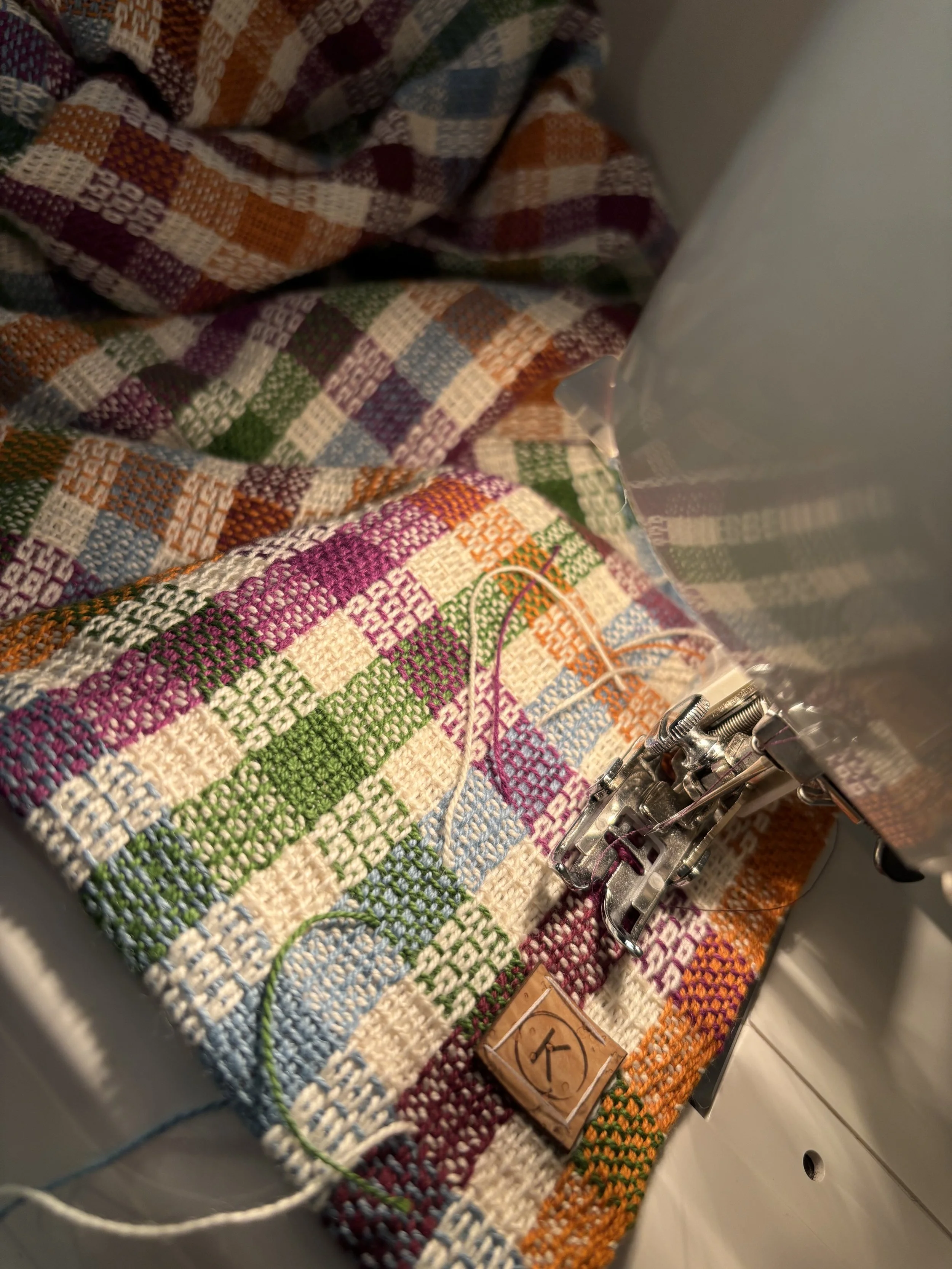 Une machine à coudre qui brode un tissu à carreaux multicolores, avec une pièce en cuir portant la lettre K.