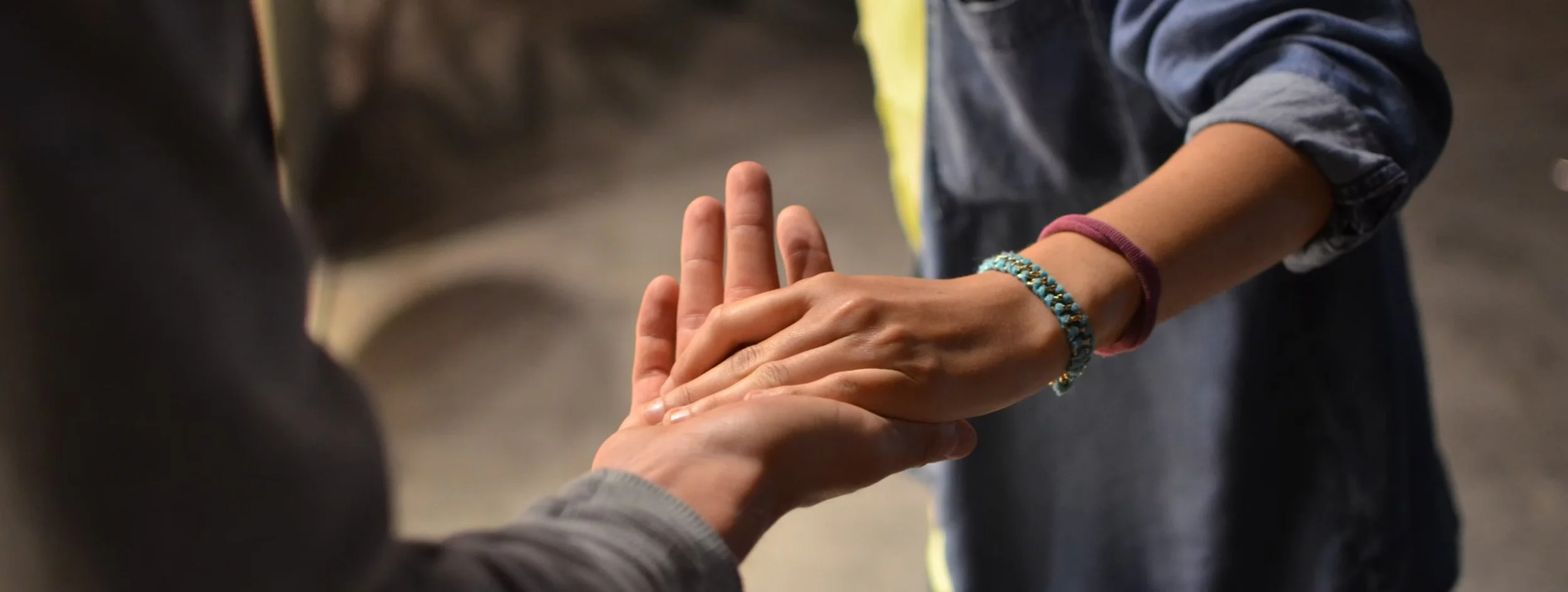 Two people holding hands, one person wearing a bracelet and a long sleeve shirt, the other person wearing a hoodie.