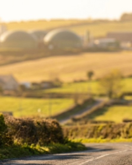 Blurry scenic landscape with rolling hills, farm buildings, and green fields.