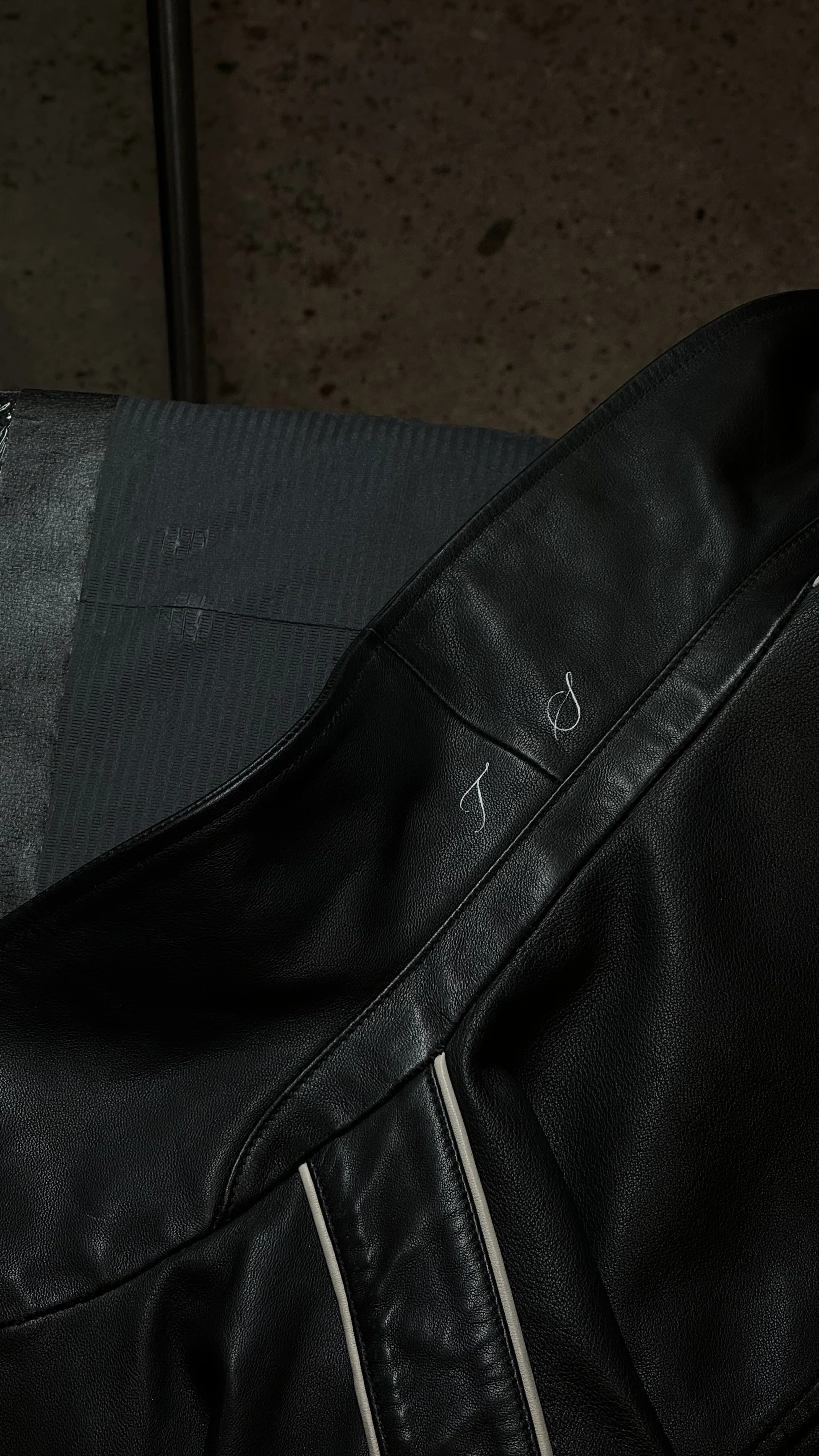 Close-up of a black leather bag with white stitching and numbers 8 and 9 written on it in white ink, resting on a textured dark surface.