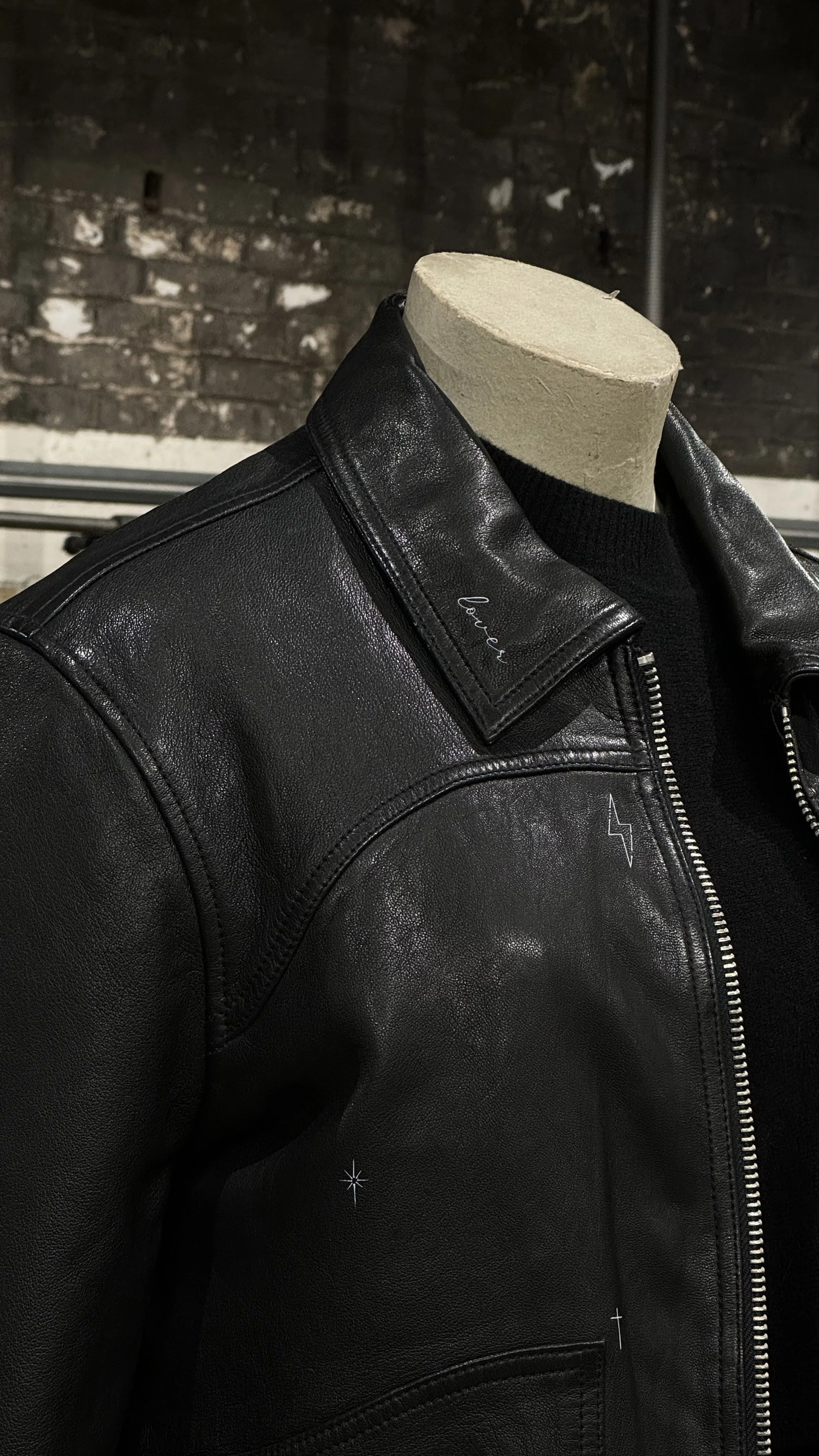Black leather jacket on a mannequin with a dark brick wall in the background.