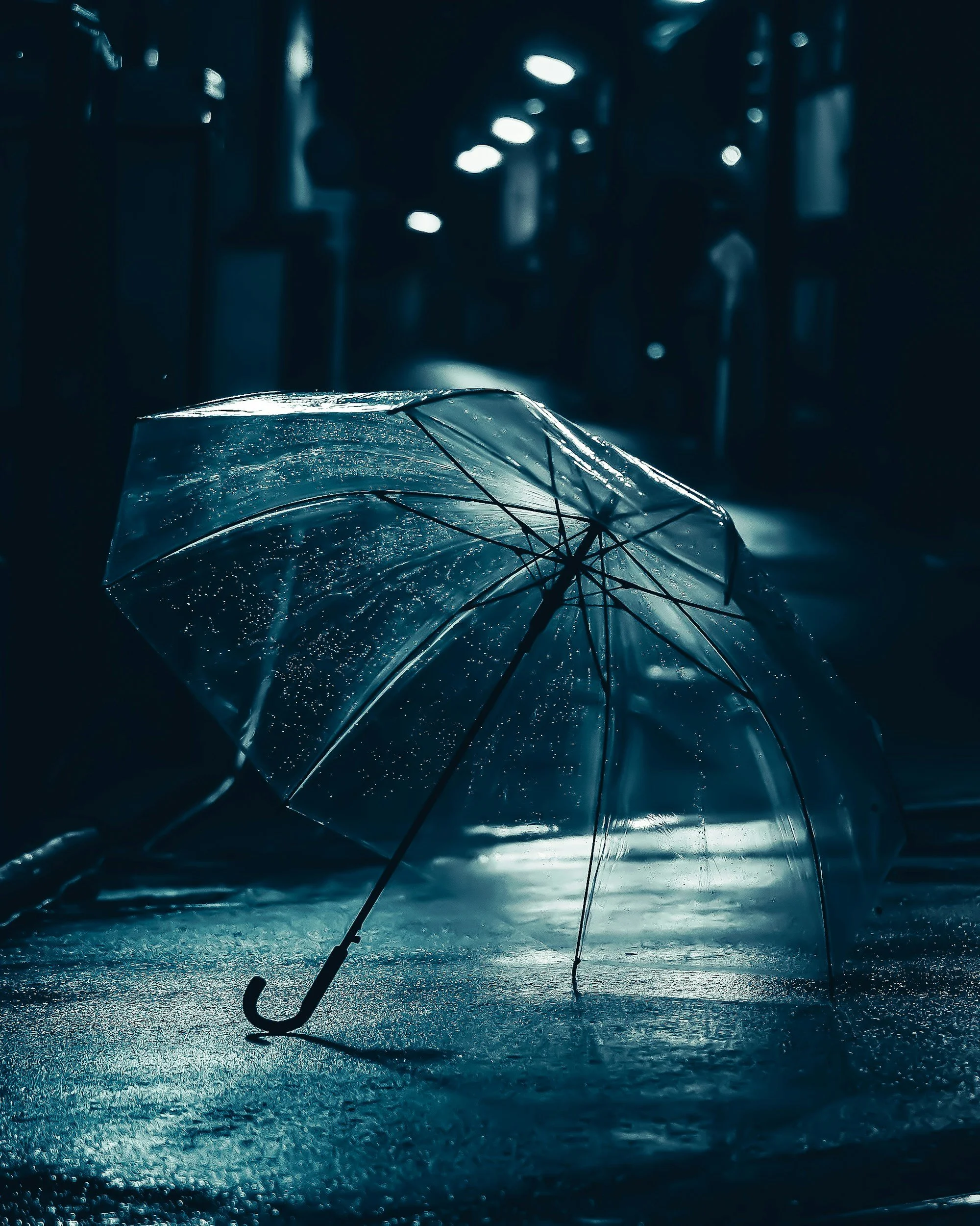 A broken transparent umbrella on a wet surface in a dark, rainy environment with bright reflections.