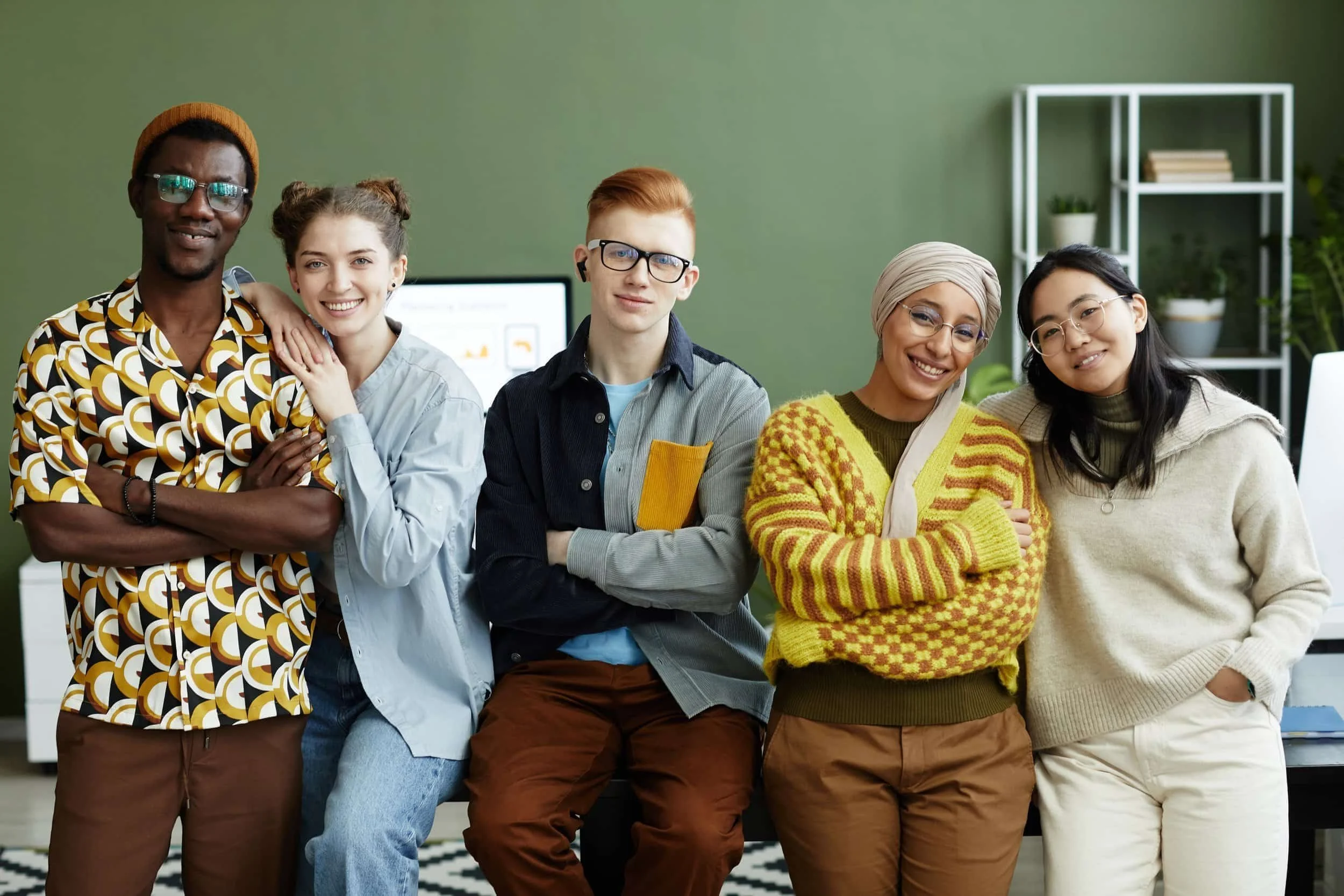Group of five diverse people smiling and standing together in an office with a green wall.