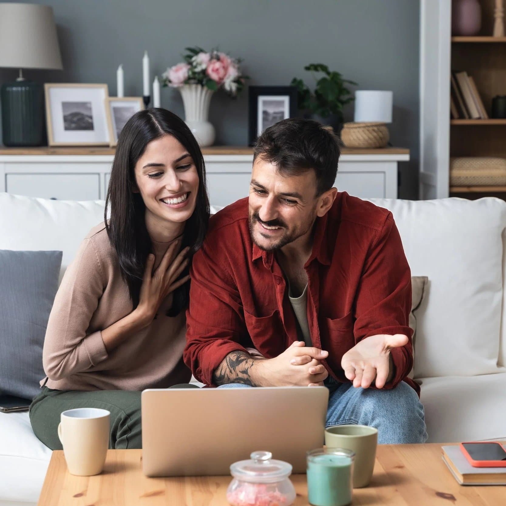 Smiling couple sits on a couch, exploring relationship focused therapy together in a cozy living room with flowers and candles.