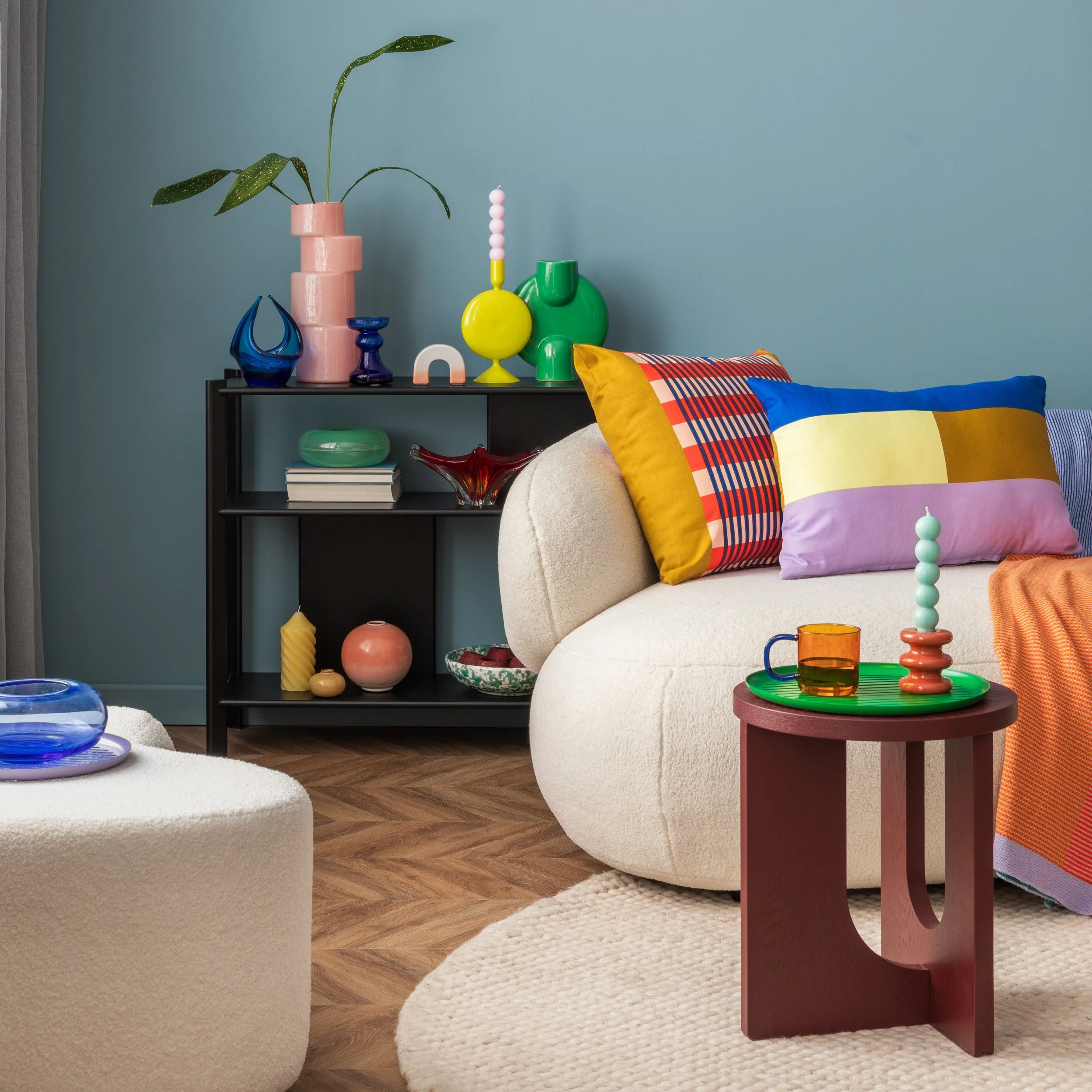Cozy therapist office with colorful cushions, vases, candles, and mugs on modern furniture against a blue wall and wooden floor.