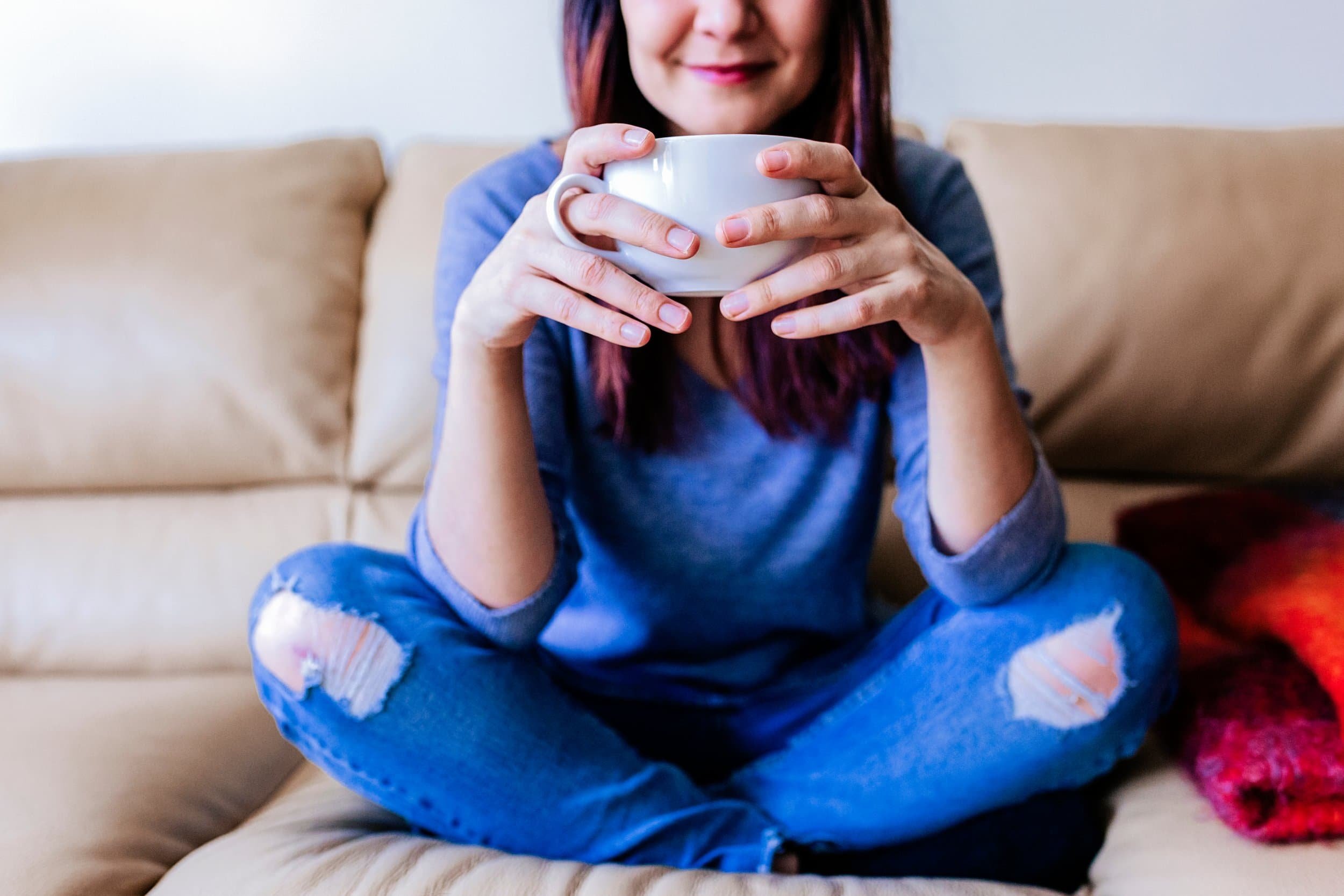 Woman sitting cross-legged on a couch, smiling with a white mug relaxed after her neurodivergent therapy session.