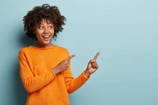 Smiling person in an orange sweater points to the right against a plain light blue background.
