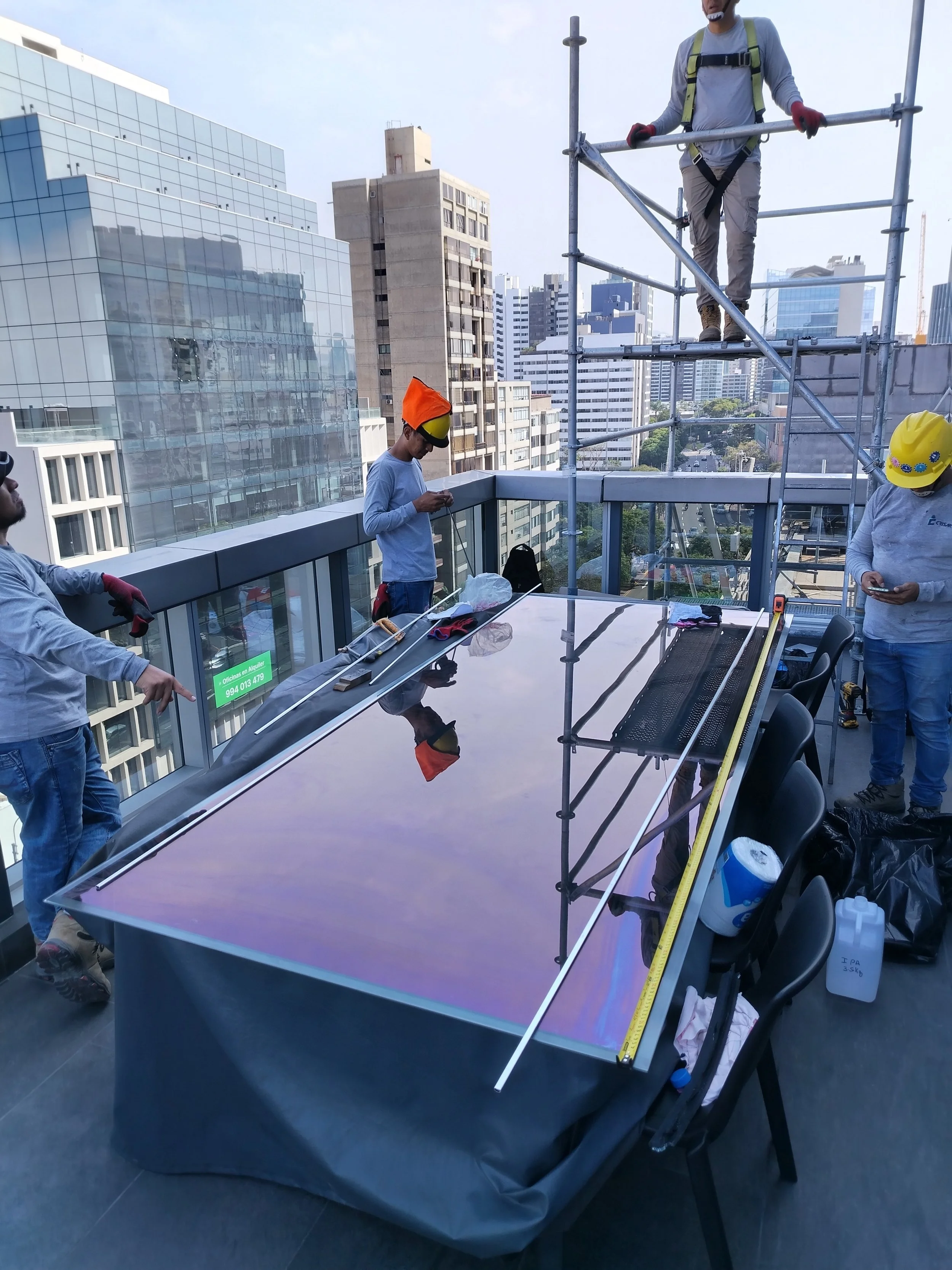 Personas trabajando en un techo con un vidrio insulado y andamios en un entorno urbano.