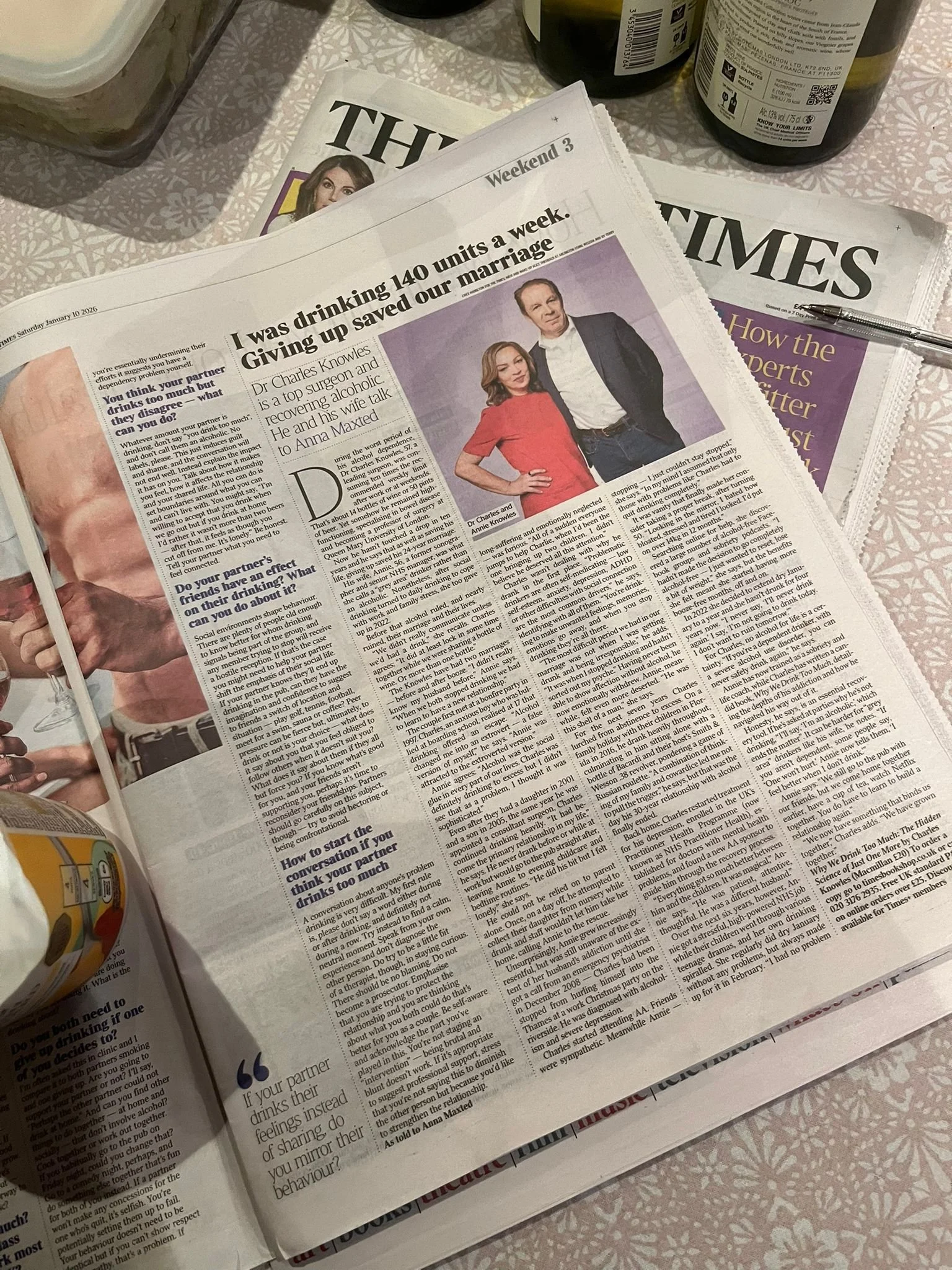 A newspaper on a table with an article about a couple, Dr. Charles Knowles and Anna Maxted, discussing their marriage and drinking habits, with a photograph of the couple and some beverages nearby.