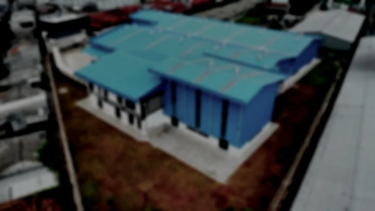 Construction site with blue buildings, green scaffolding, and yellow cranes under a cloudy sky.