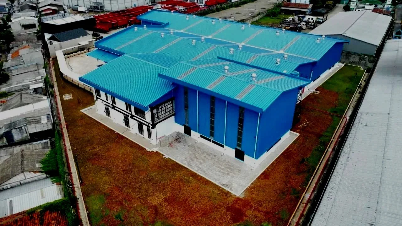 Construction site with blue buildings, green scaffolding, and yellow cranes under a cloudy sky.