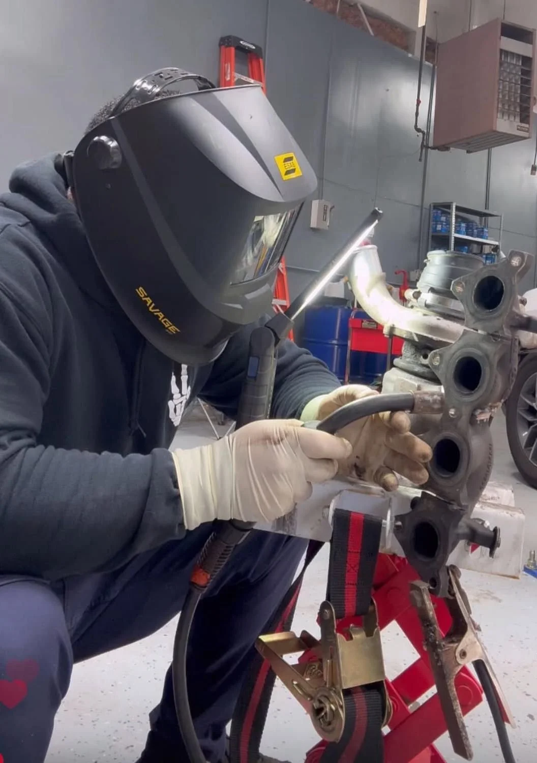 Un mecánico usa un casco de soldar y guantes, trabaja en un motor en un taller mecánico.