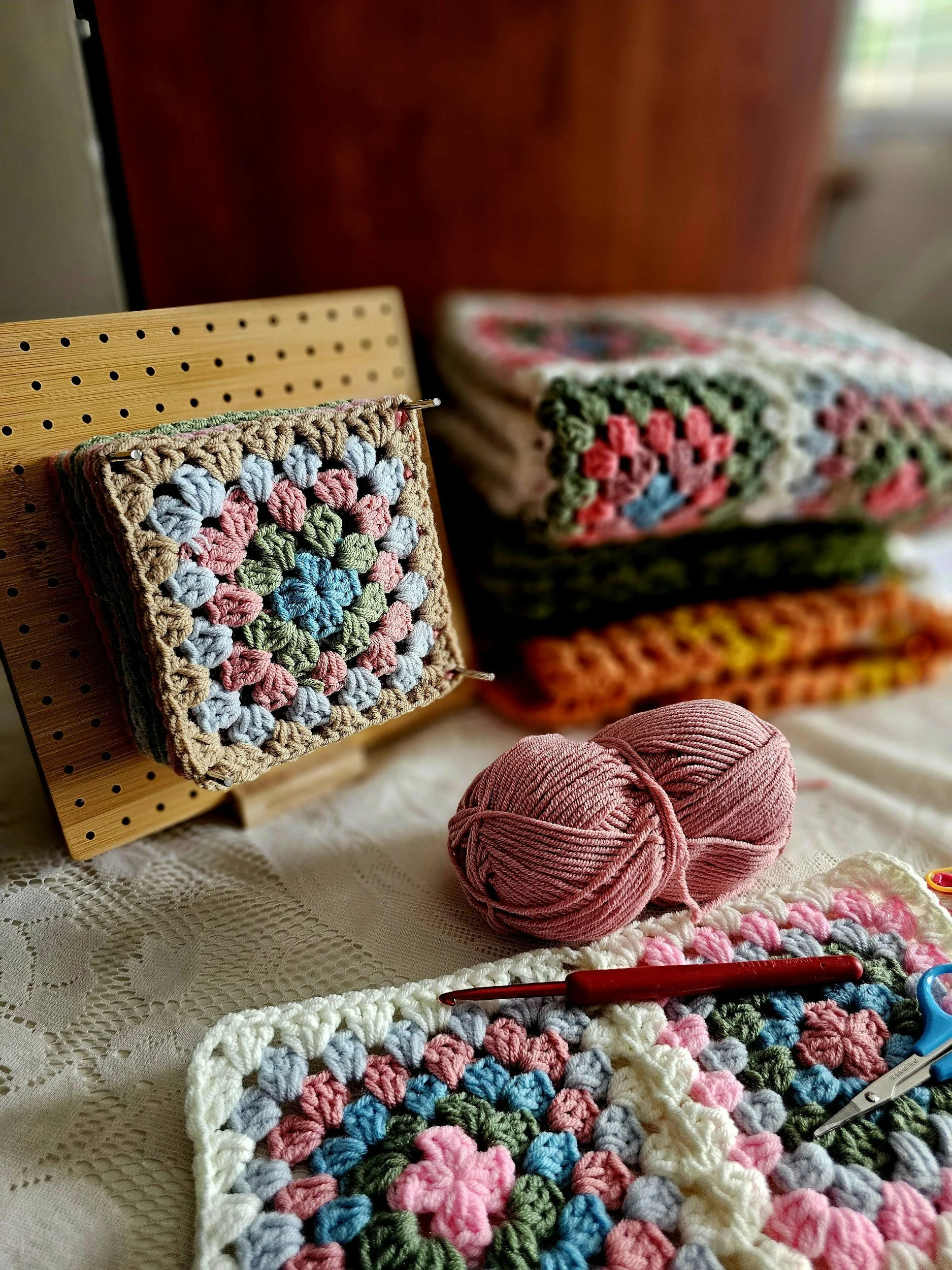 Crochet squares and yarn on a table, with crochet tools and completed patterns.