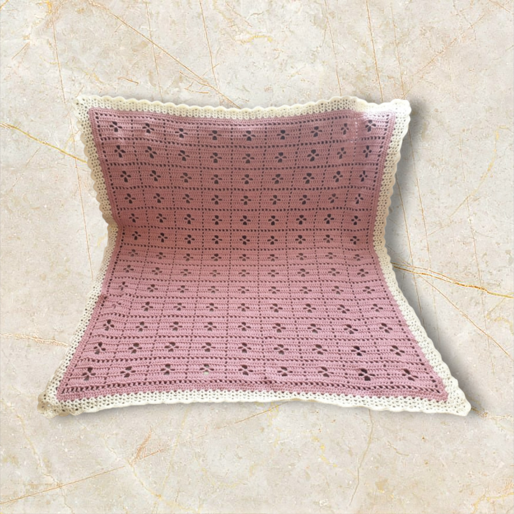 A pink crocheted pillow with a white border layered over a light-colored, textured surface.