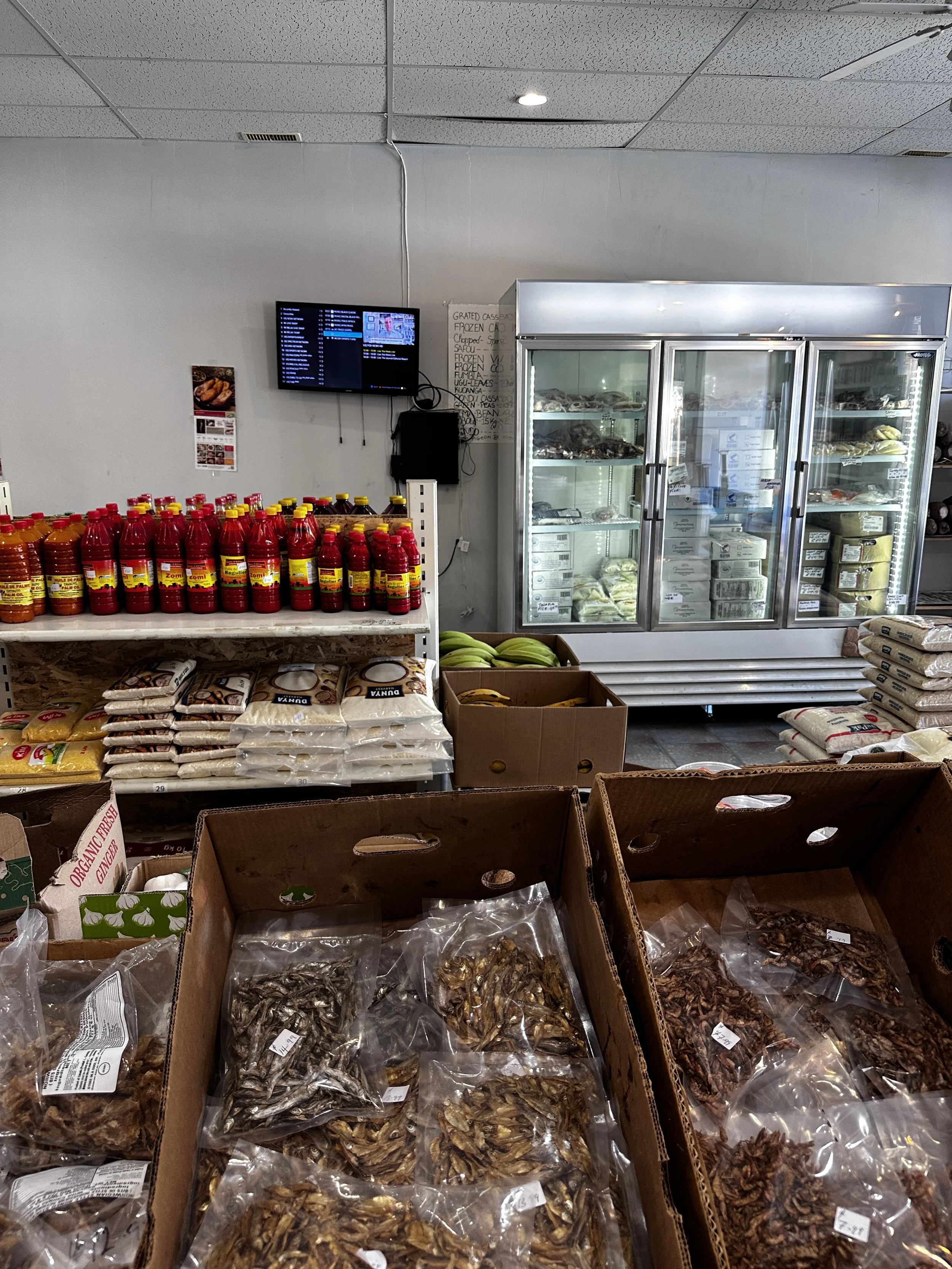 Shelf stocked with sauces, rice, and bananas next to a cooler with frozen items, in a grocery store.