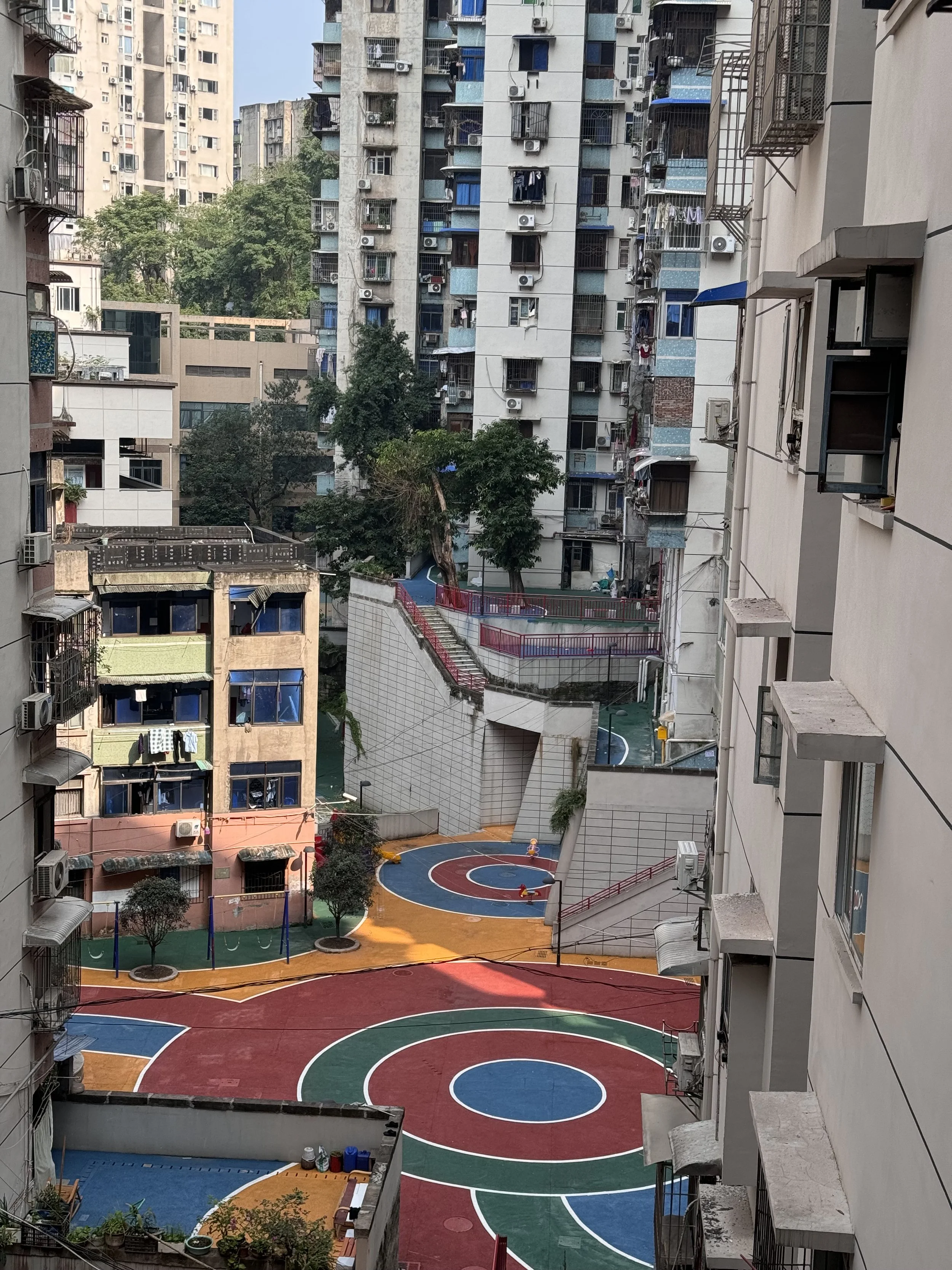 View of residential high-rise buildings surrounding a colorful playground with basketball courts and trees.