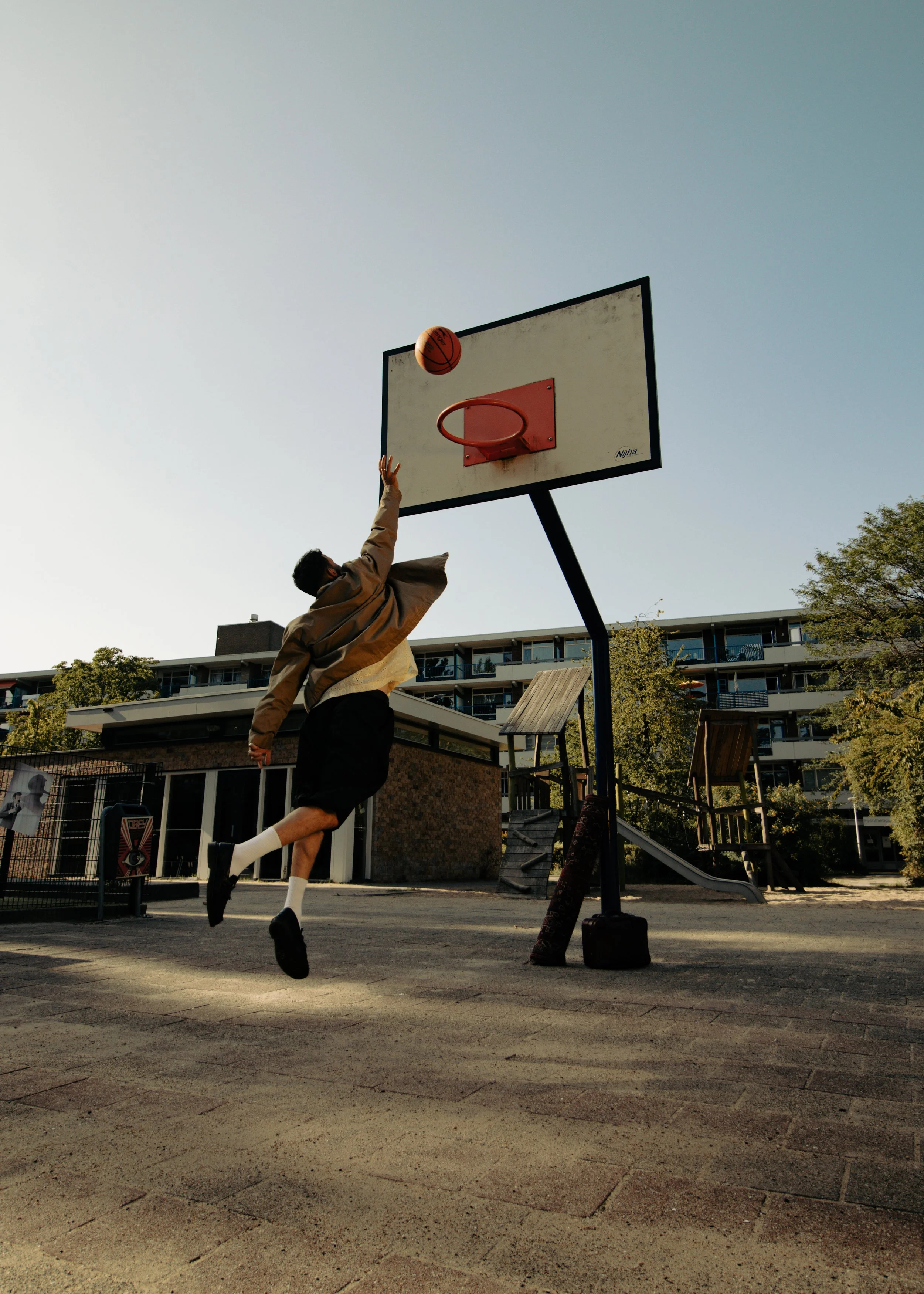 A person playing basketball outdoors, jumping to shoot the ball towards the hoop.