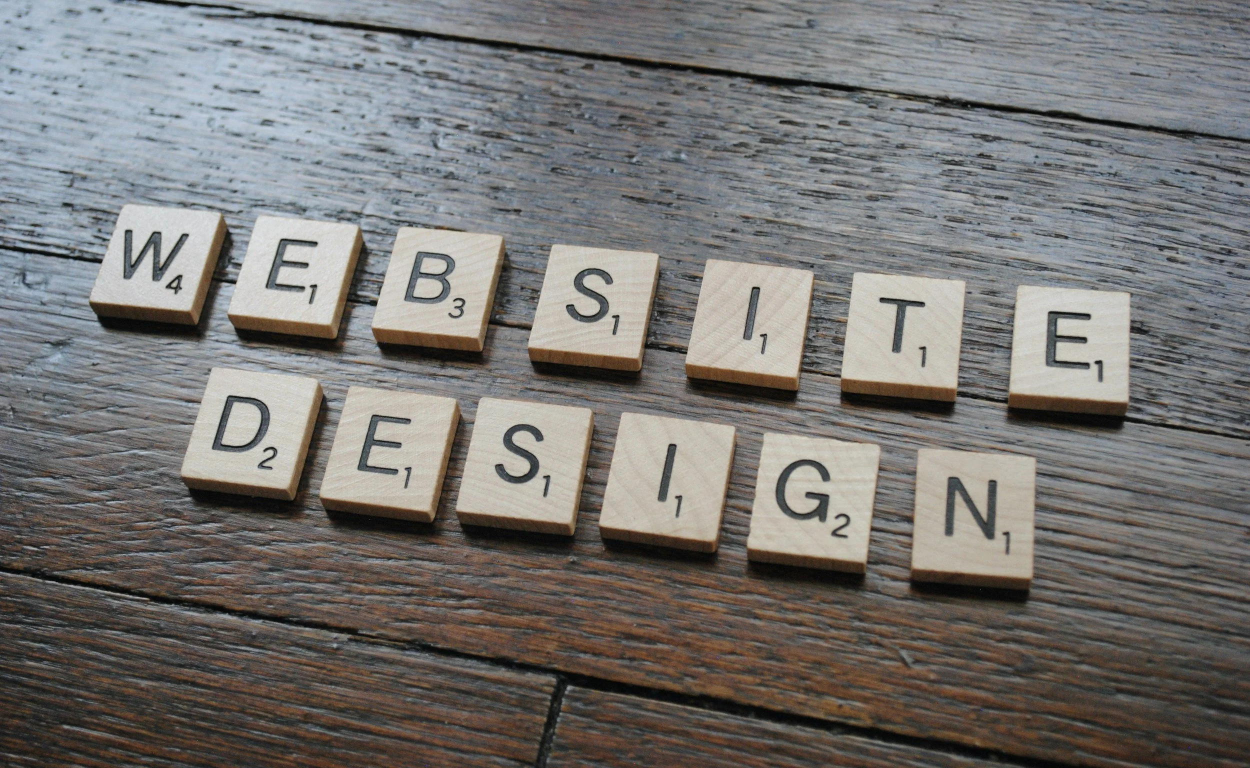 Scrabble tiles spelling out 'WEBSITE DESIGN' on a wooden surface.
