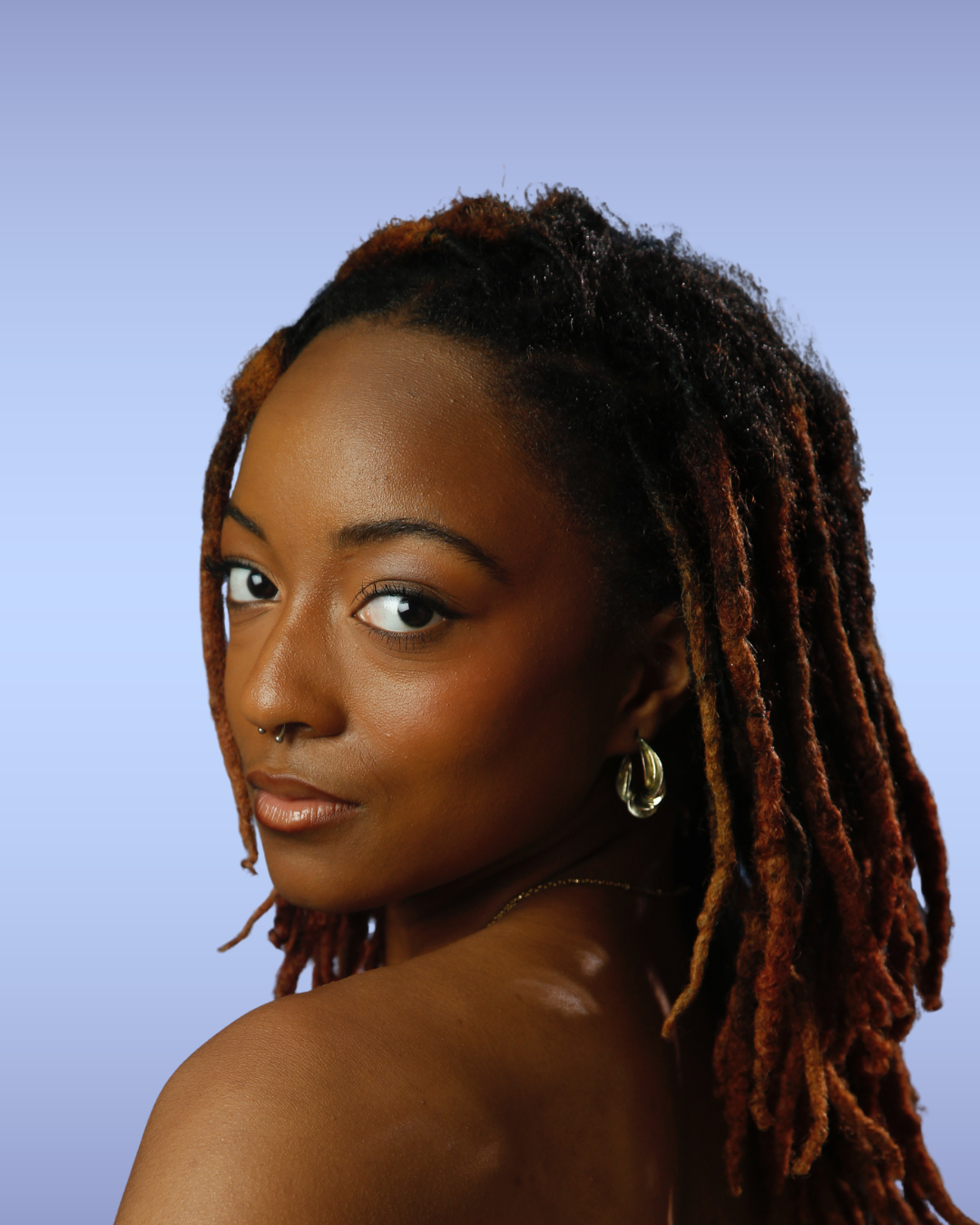 Close-up portrait of a woman with dreadlocks, wearing earrings and a septum piercing, with a neutral expression against a gradient background.