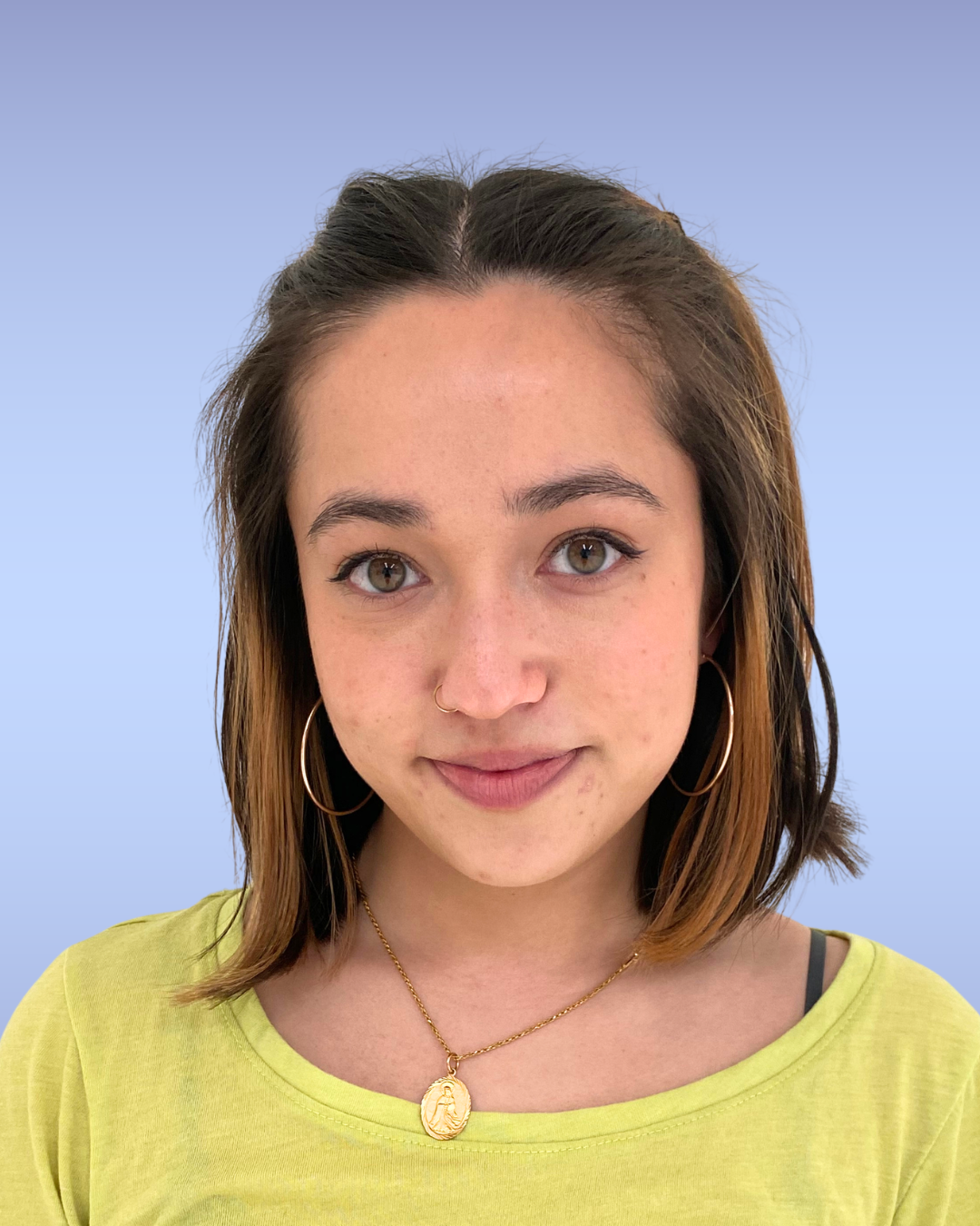 Close-up of a young woman with black hair, hazel eyes, and tan skin, wearing gold jewelry including hoop earrings, a necklace, and a small nose ring, against a light blue background.