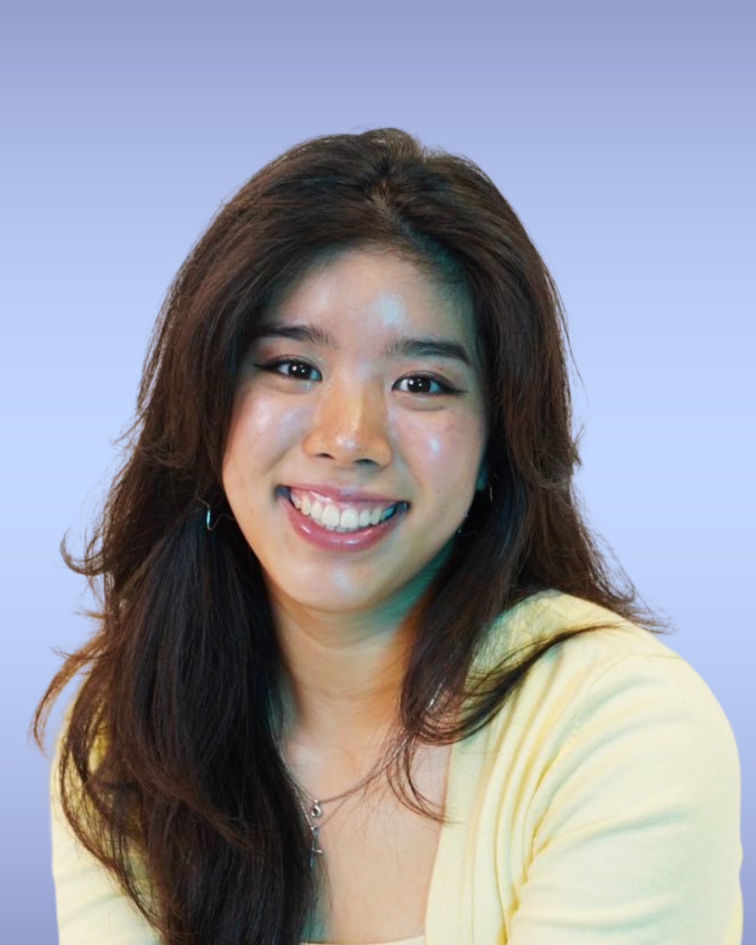 Portrait of a young woman with long dark hair, smiling, wearing a yellow top and a necklace, against a light blue background.