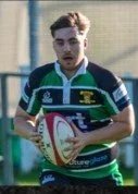 A young man in a green and black sports jersey holding a rugby ball.