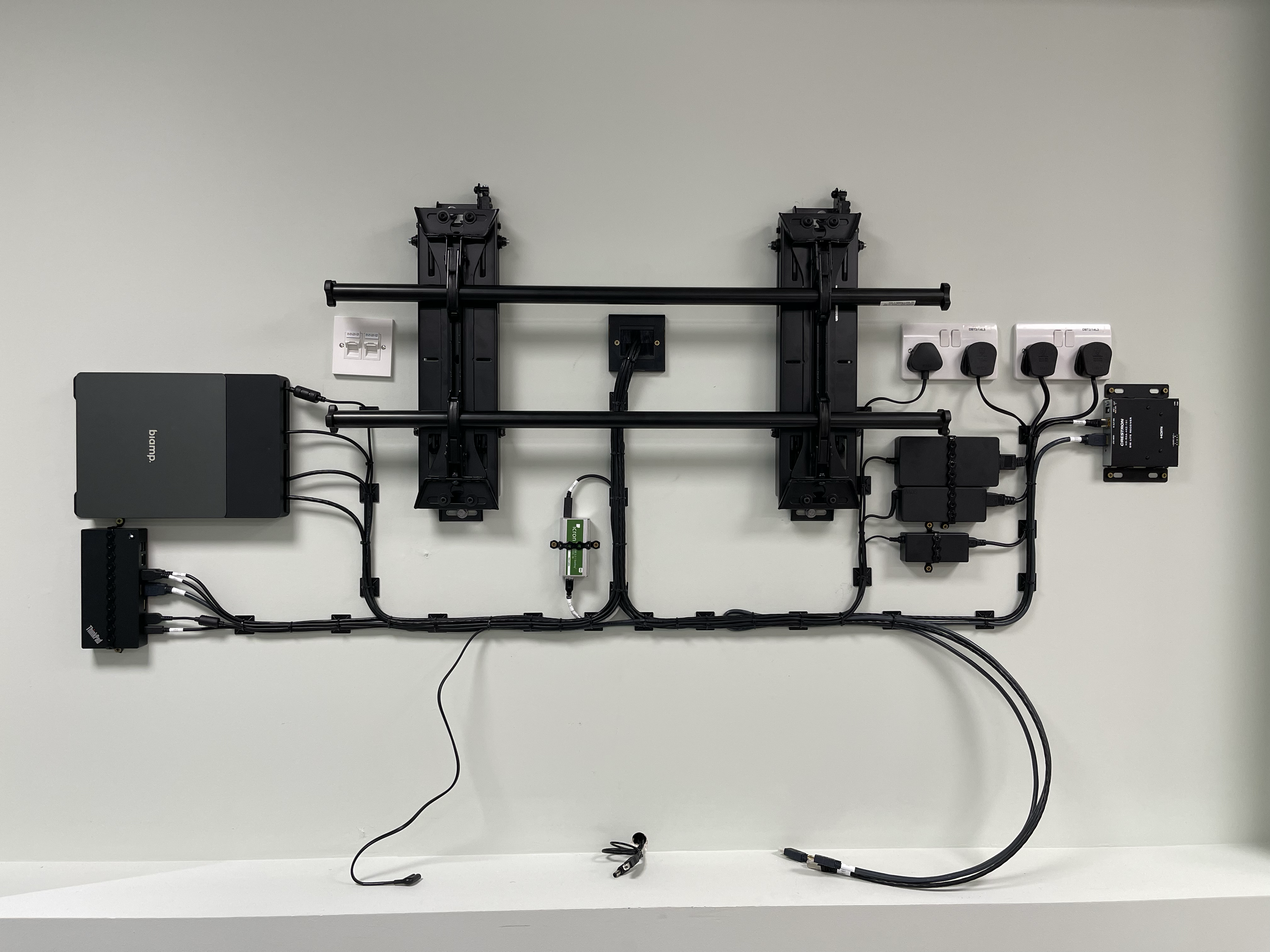 Wall-mounted electronic equipment layout including power supplies, cables, and mounting hardware on a plain white wall.