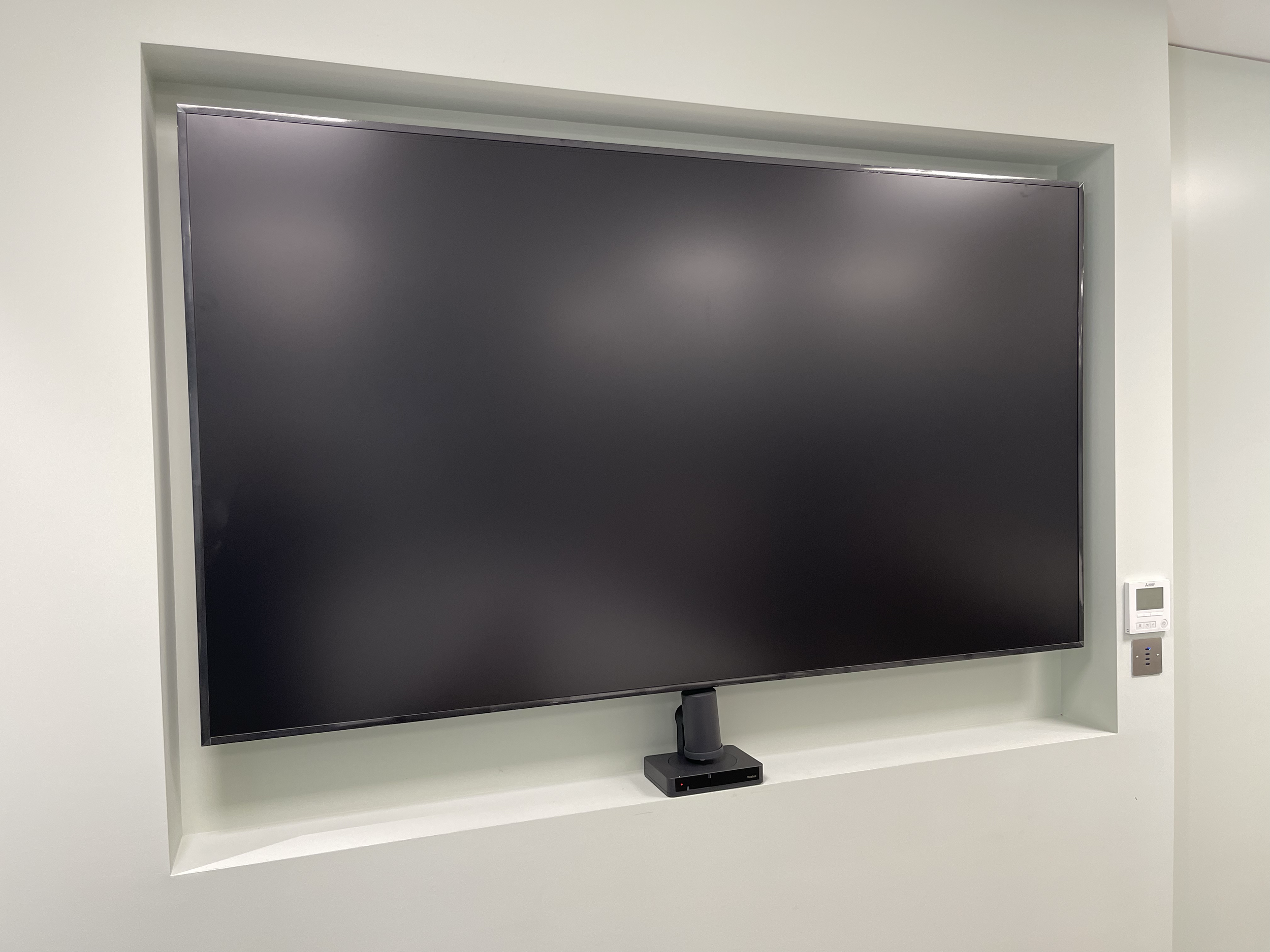 Large flat-screen television mounted in a recessed wall with a control panel to the right.