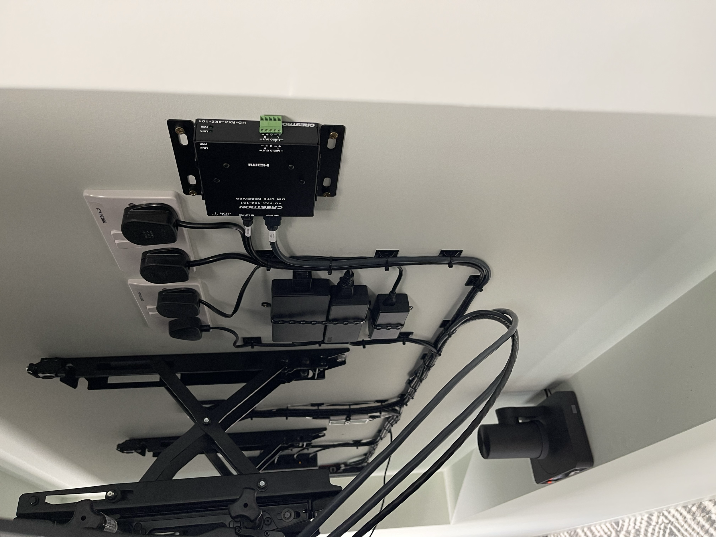 Electrical and mechanical components mounted on the underside of a desk or table, including power outlets, wiring, and a motorized lift mechanism.