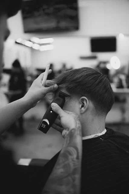 A person getting a haircut at a salon, with a barber using clippers to trim the hair of a male customer. INV8 Hair best Chicago barbers