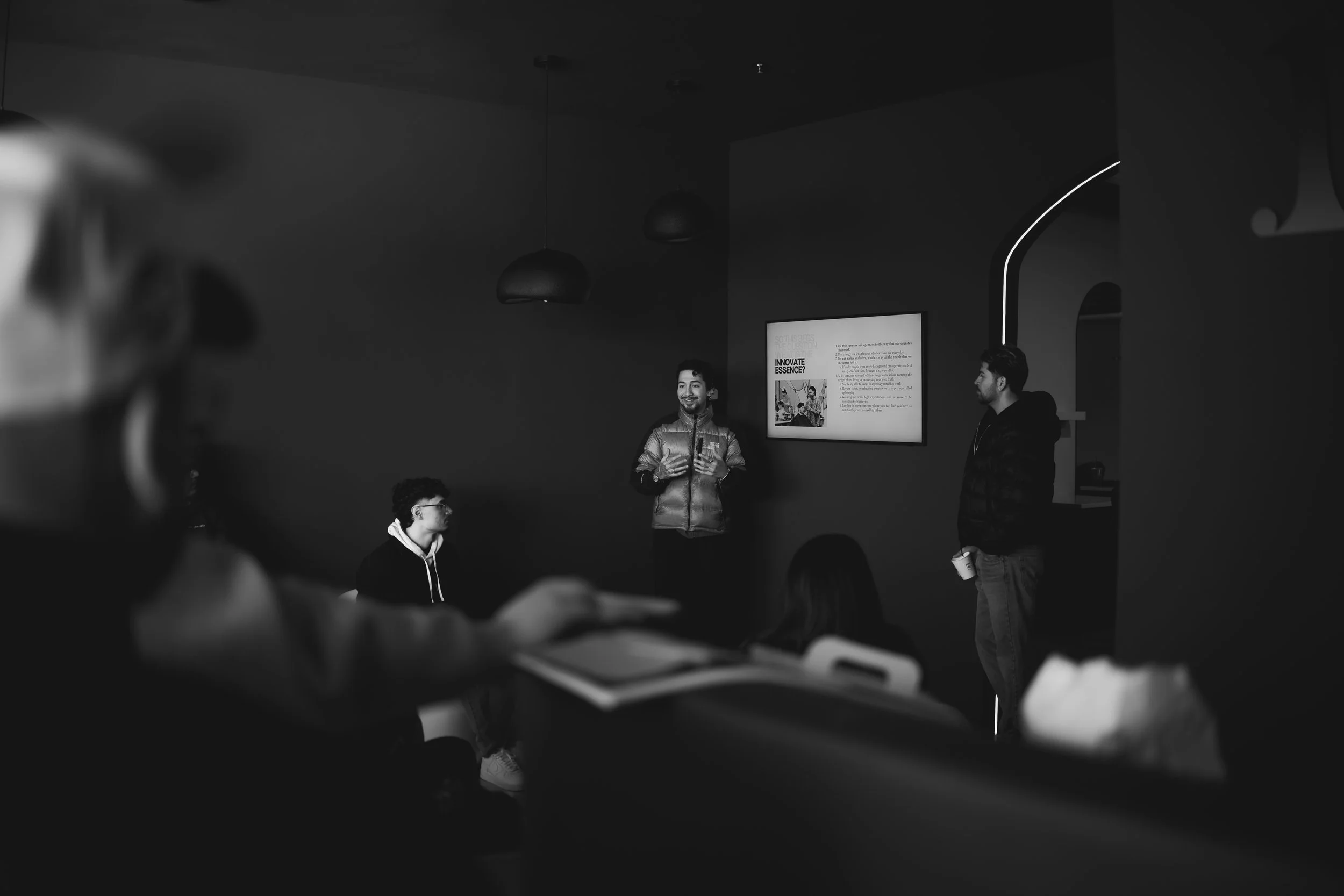 A man presents to a small group in a dark room with a digital screen on the wall.