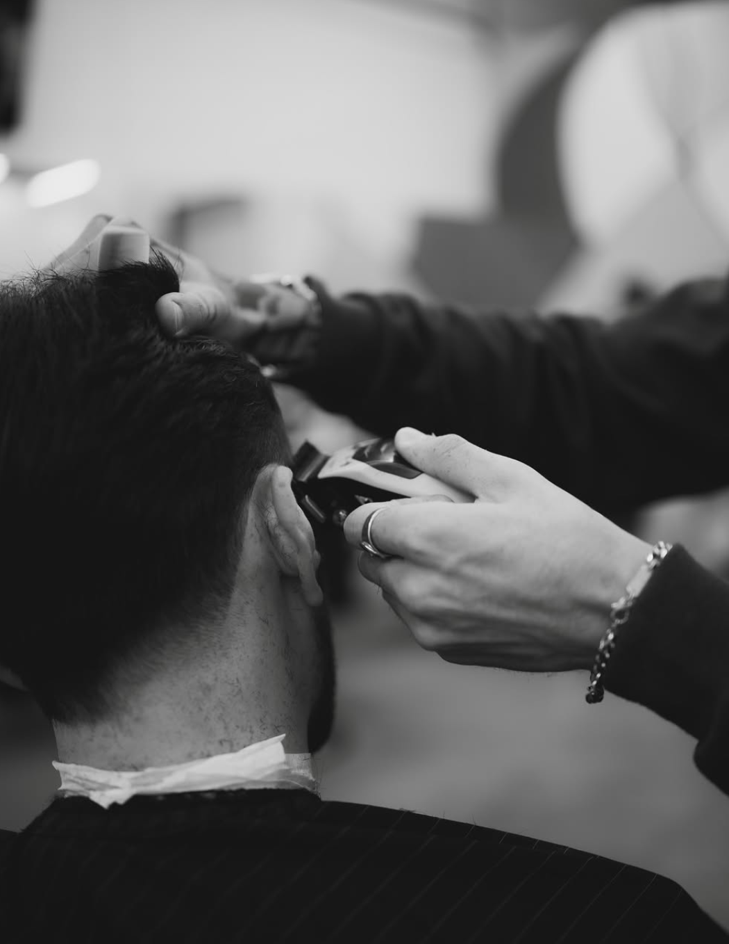A person shaves another person's face, with a focus on the hand holding the razor and the person's ear and neck visible, in a close-up black and white image. Barber in the Chicagoland area.