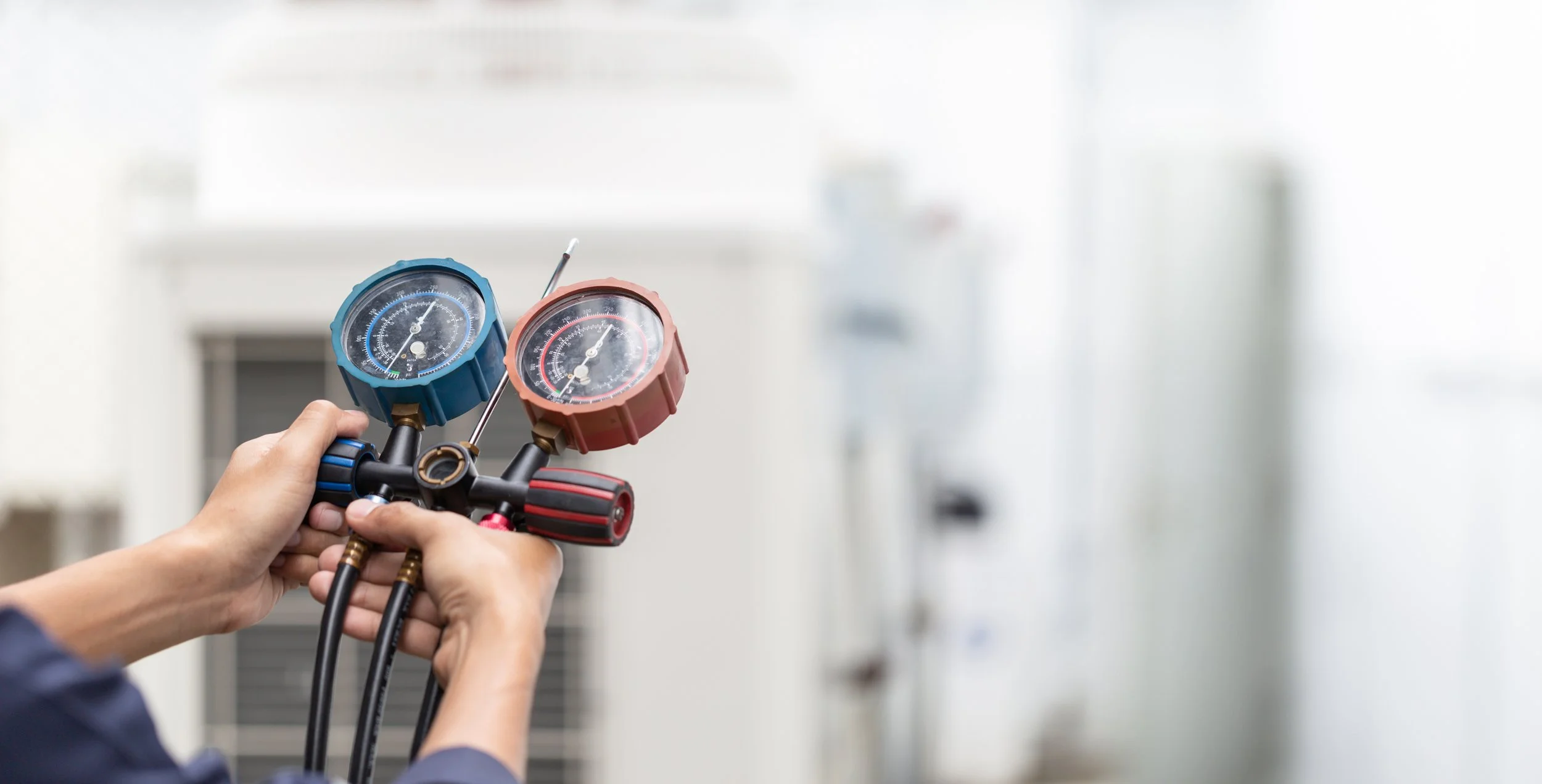 Person holding manifold gauge set with blue and red gauges for HVAC system testing.