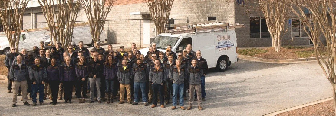 Group of people standing outdoors in front of a service van with trees and a building in the background.