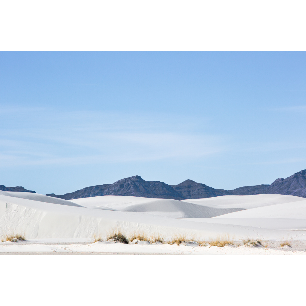 Expansive white gypsum dunes with distant mountains beneath a clear sky in White Sands National Park.
