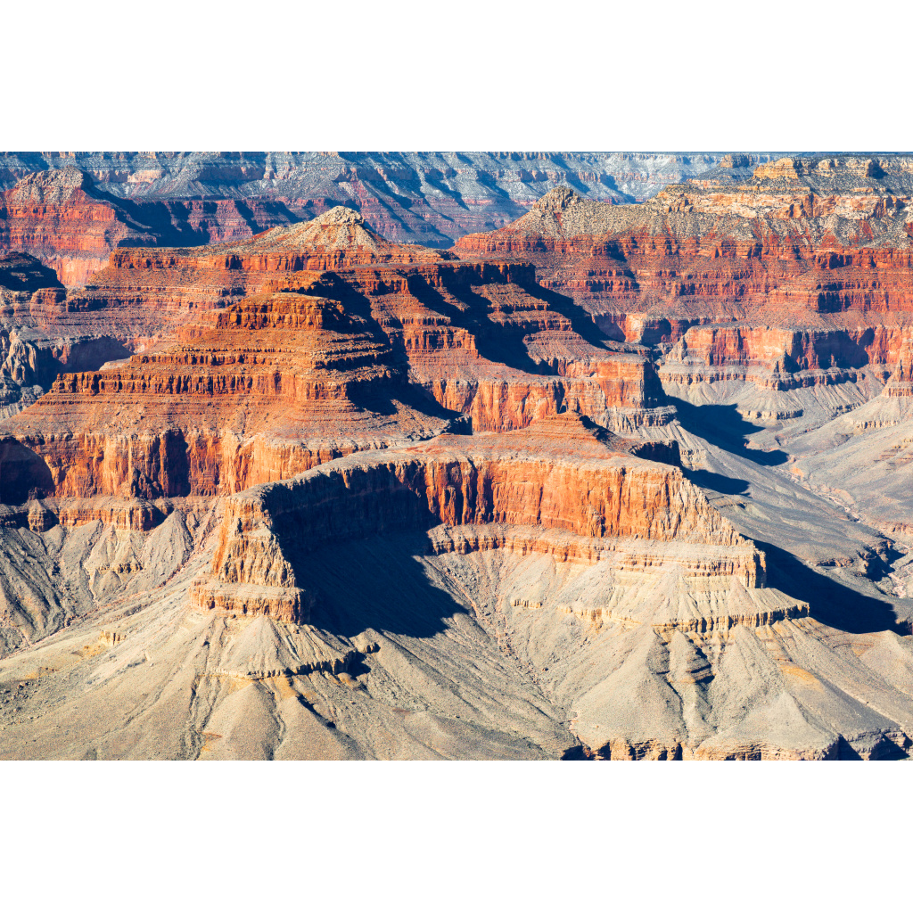 Panoramic view of layered sandstone mesas and buttes in the Grand Canyon under warm desert light.